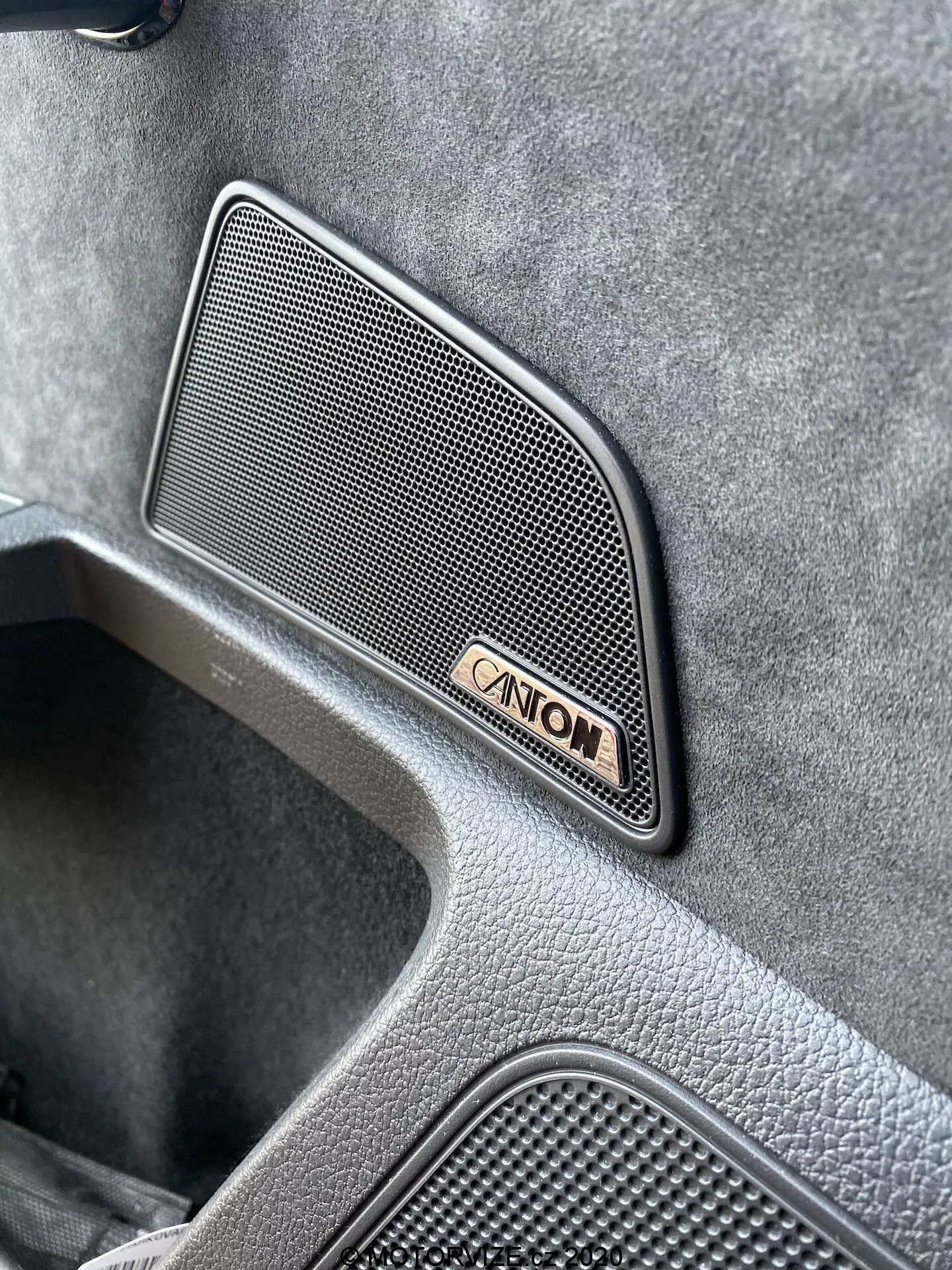 Vista angular de primer plano del interior del Skoda Superb Limousine 2019, destacando una rejilla de altavoz de audio Canton premium con forma trapezoidal de patrón de malla, ubicada en el panel de la puerta, acompañada de la insignia Canton, que muestra un acabado texturizado de alta gama y un área empotrada indicativa de un diseño de vehículo lujoso.
