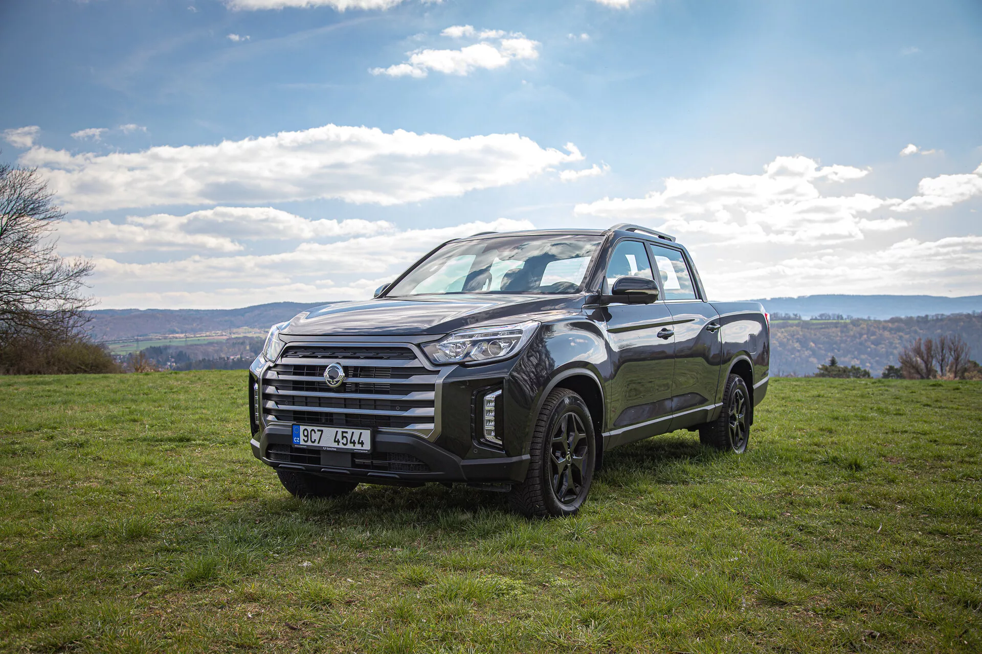 Camioneta SsangYong Musso Grand 2022 aparcada en un paisaje con césped bajo un cielo nublado, mostrando su diseño robusto y capacidad todoterreno con vista frontal de tres cuartos durante el día.