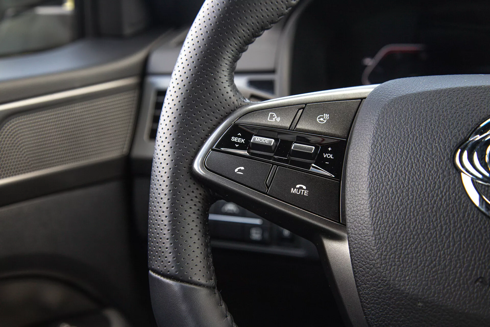 Vista detallada de los controles en el lado izquierdo del volante del SsangYong Musso 2022 con agarre de cuero perforado y botones de tecnología montados para la comodidad y seguridad del conductor
