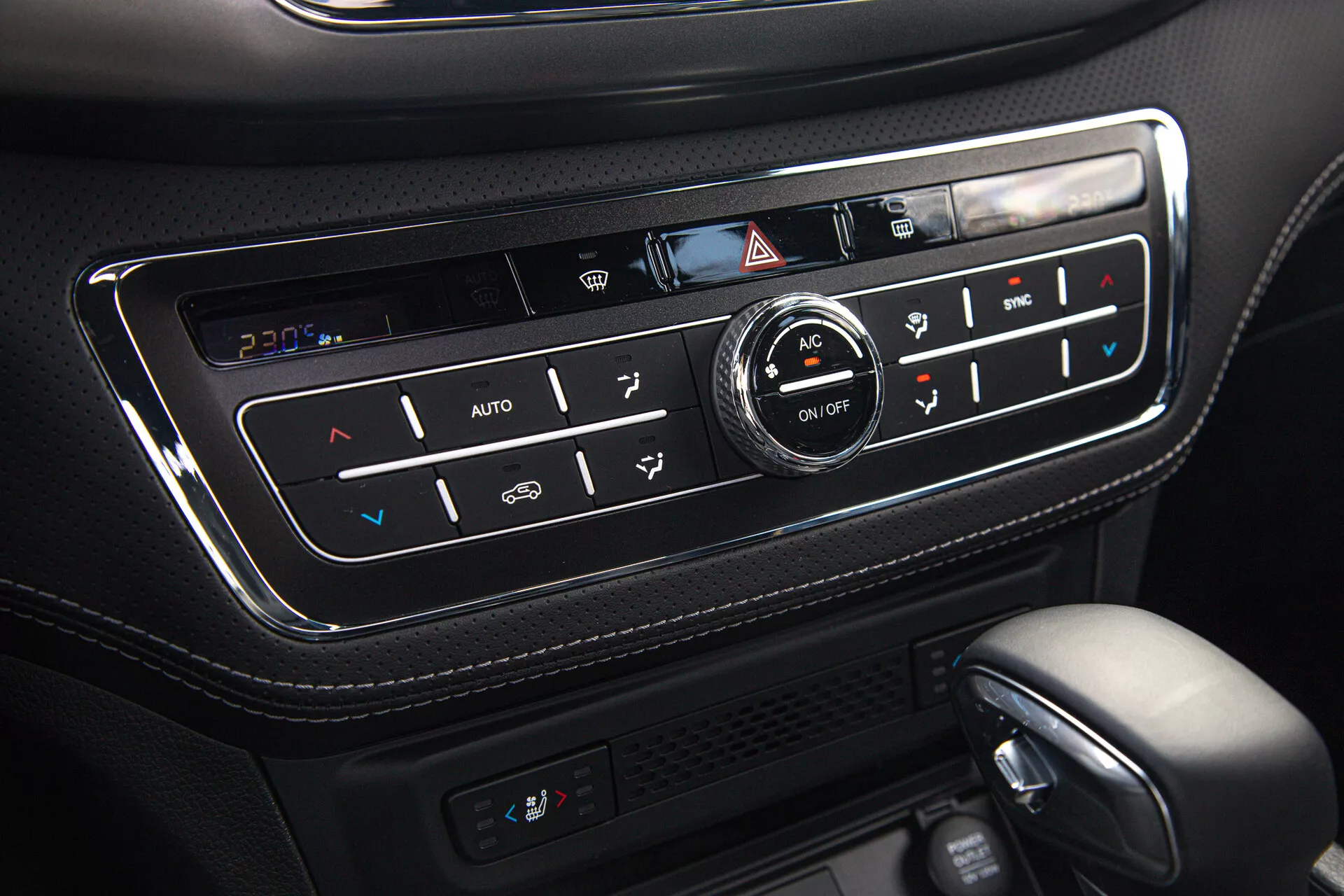 Vista de cerca del panel de control climático del SsangYong Musso 2022 Grand Pick-up mostrando el sistema de ajuste automático de temperatura, control de zona dual, funcionalidad de asientos calefactados, configuraciones de AC y descongelamiento, enclavado en una consola de cuero negro de alta calidad con acabado brillante y botones retroiluminados