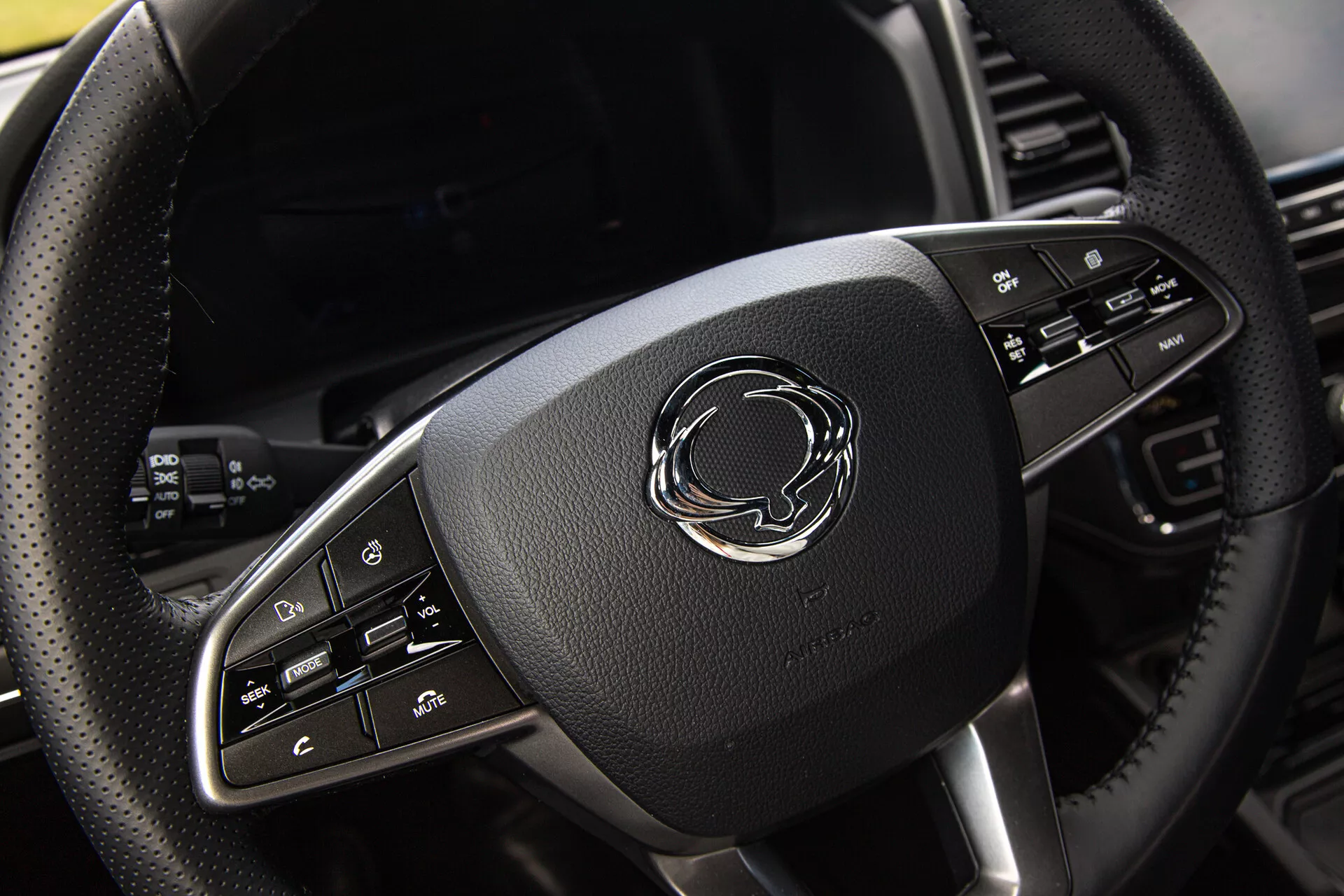 Vista cercana del volante del SsangYong Musso Grand 2022 con revestimiento de cuero, acentos cromados y botones de control avanzados