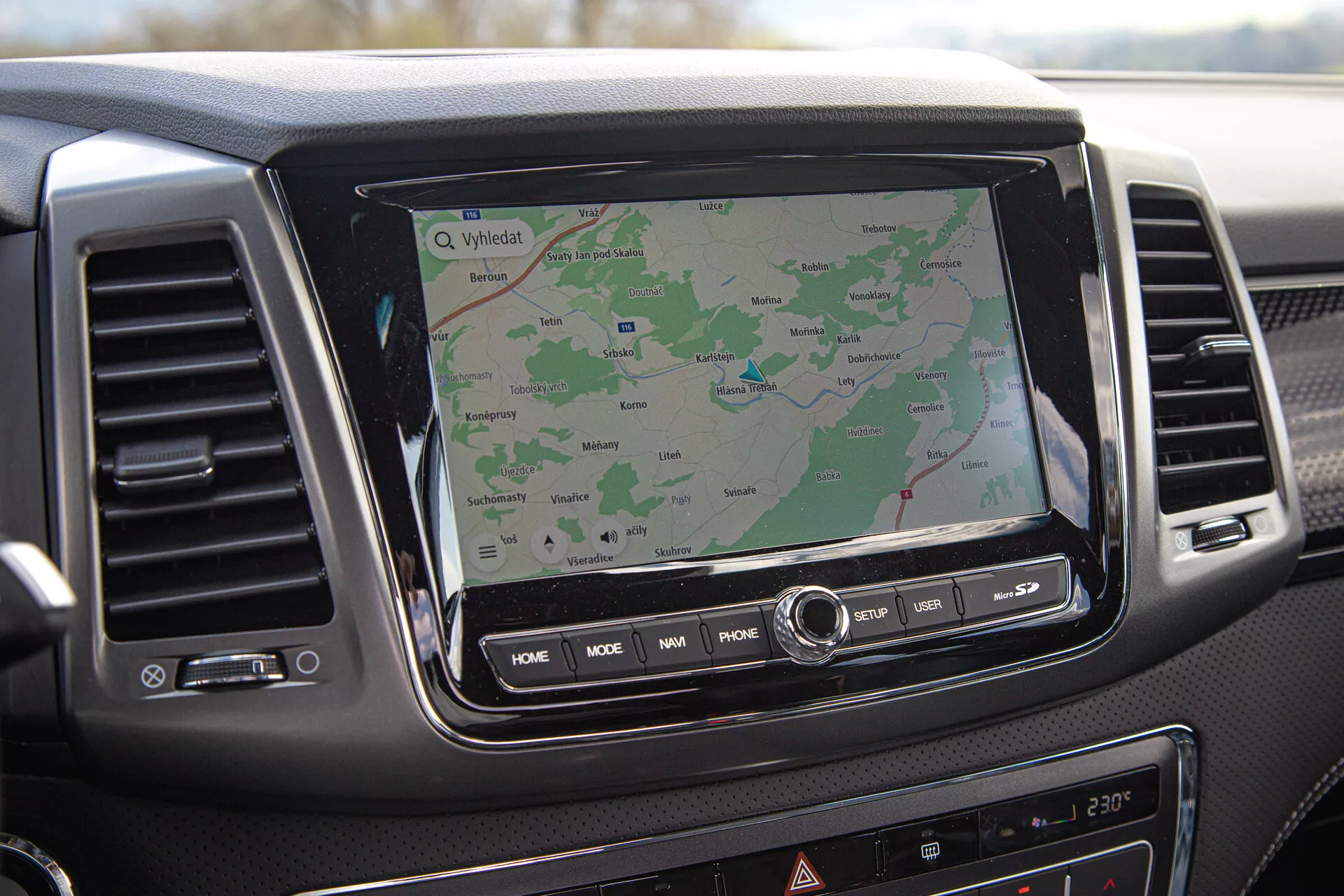 Tablero de SsangYong Musso 2022 mostrando sistema de infoentretenimiento con pantalla táctil y navegación GPS, rejillas de ventilación y botones de control, visto desde la perspectiva del pasajero.