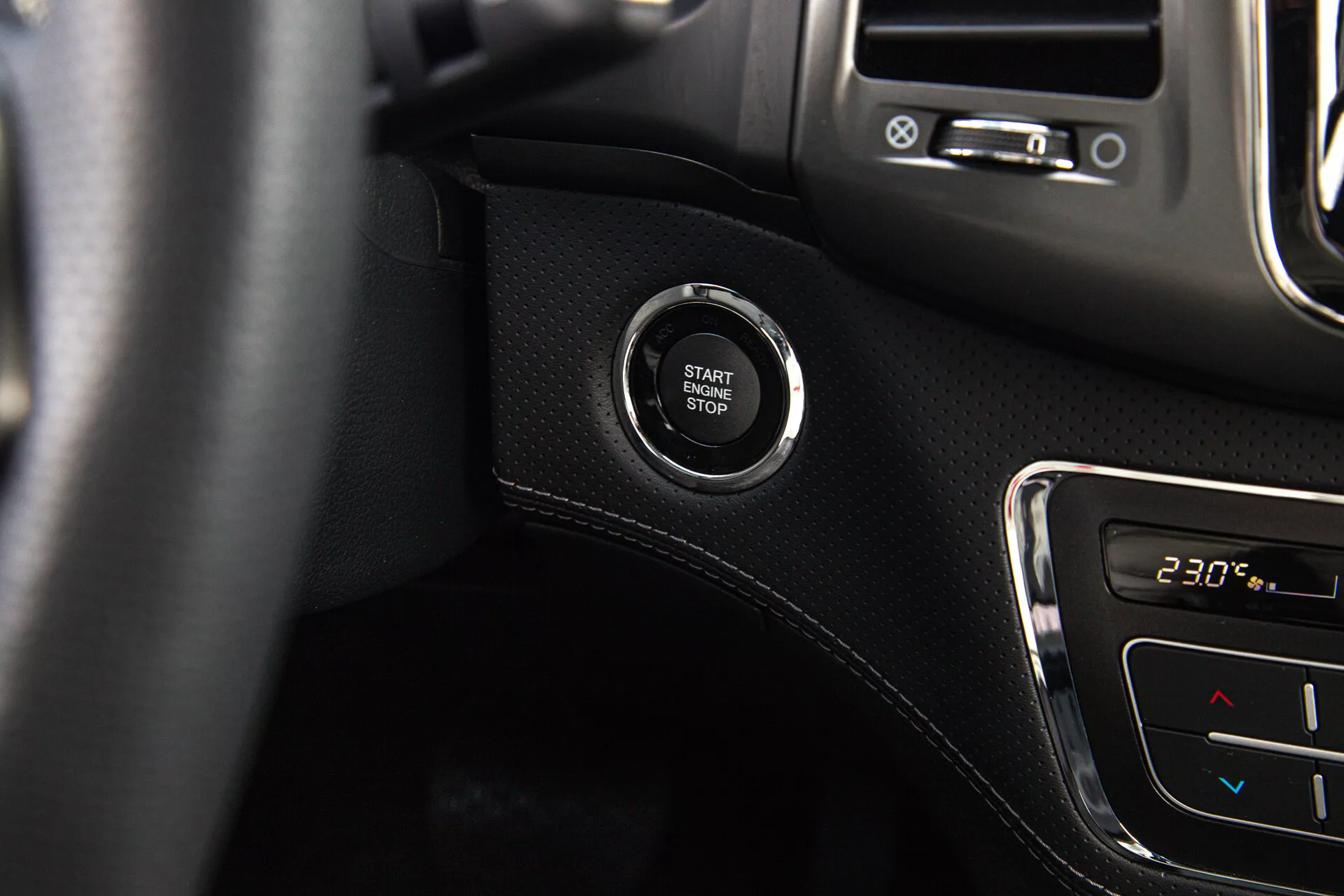 Vista de cerca del botón de arranque/parada del motor en un SsangYong Musso 2022, destacando el sistema de encendido sin llave en el tablero con superficie negra de fondo y detalles de control climático