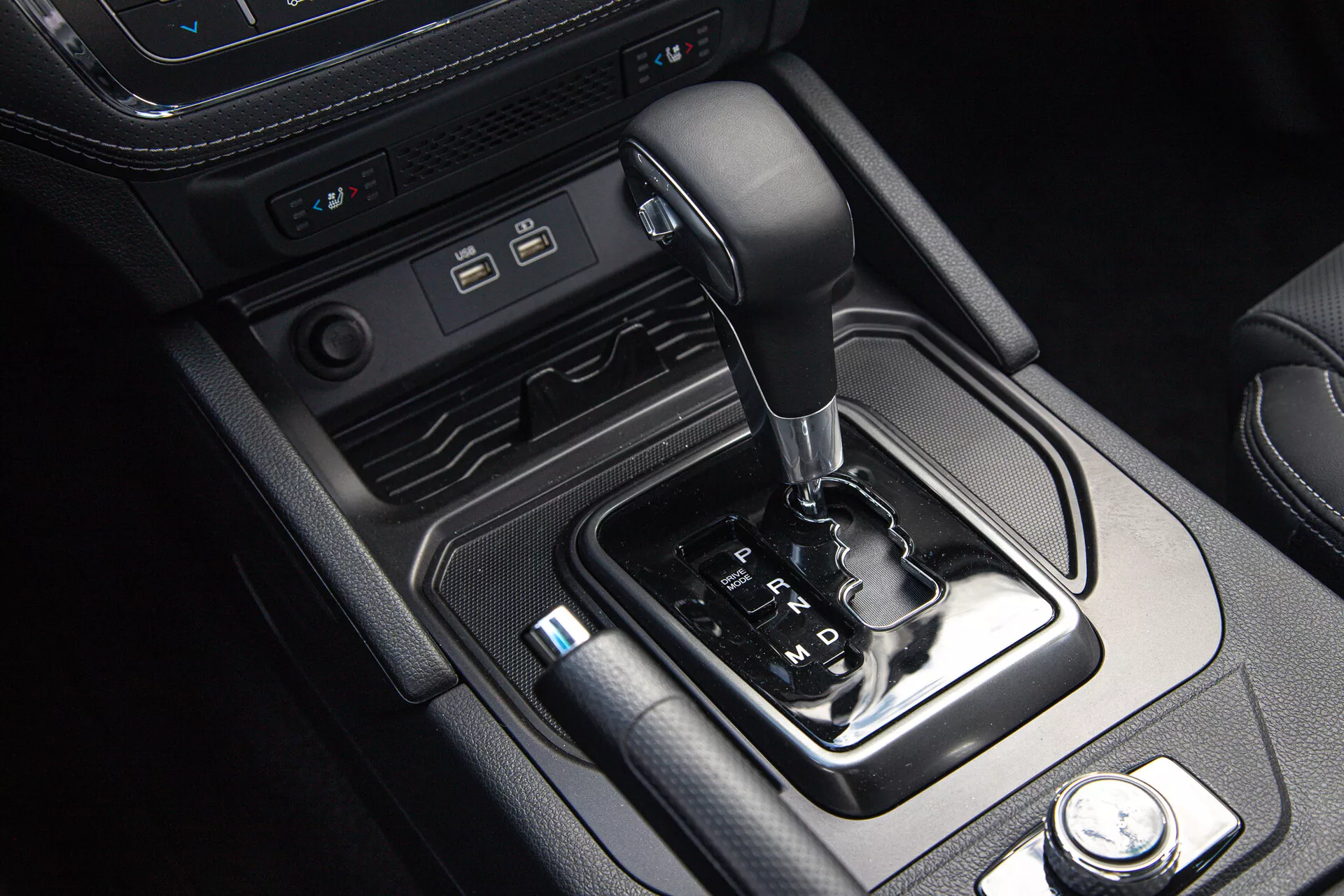 Interior del SsangYong Musso Grand Pickup 2022 mostrando consola central con selector de marchas automático, puertos de conectividad modernos y controles de modo de conducción, enmarcado por acentos de cuero y metal