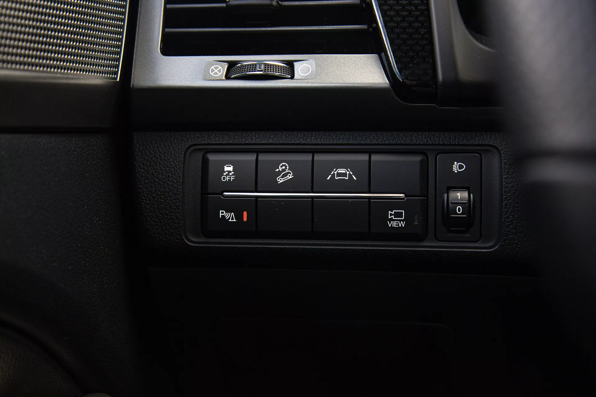 Primer plano de los controles interiores del SsangYong Musso 2022, con botones retroiluminados para control de estabilidad, capacidad fuera de carretera, asistencia de estacionamiento o carril, posición ajustable del asiento e información del sistema