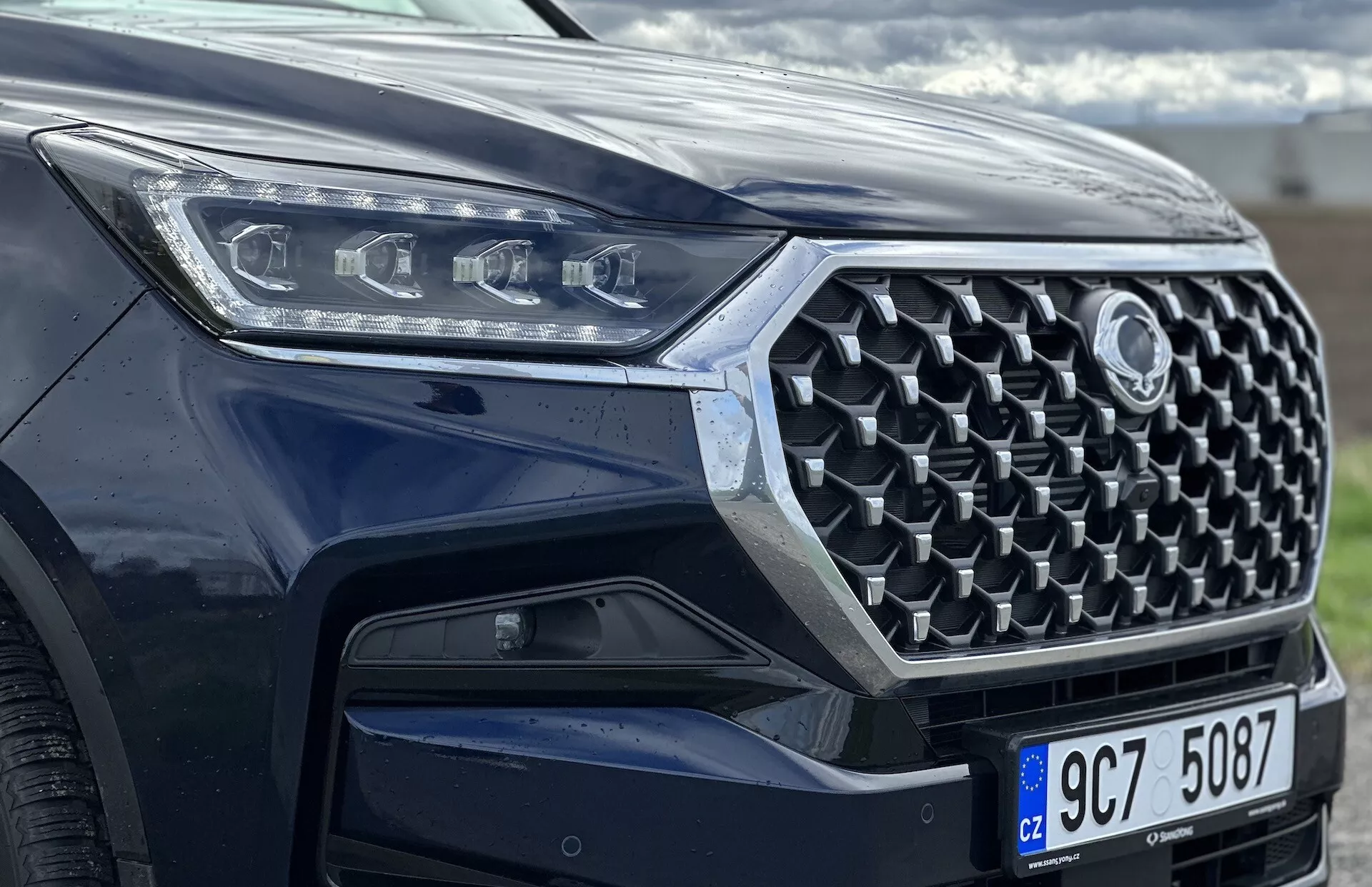 Vista frontal en ángulo del SsangYong Rexton 2021 enfocada en la parrilla, el parachoques delantero y el diseño de las luces de cabeza LED, mostrando características de seguridad avanzadas y tecnología moderna con pintura metálica.