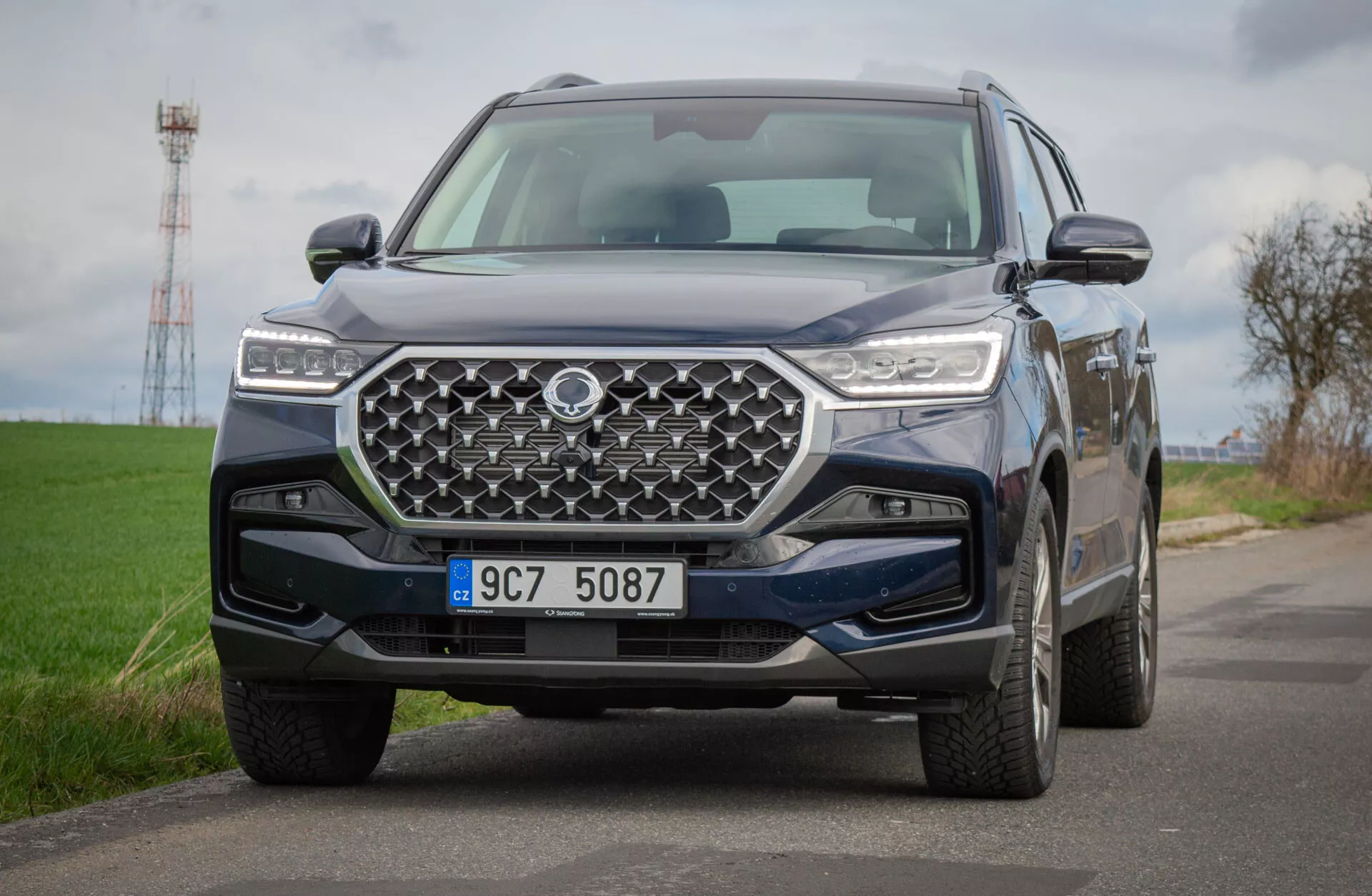 SUV SsangYong Rexton 2021 en camino rural, mostrando una vista detallada de su diseño frontal con una parrilla geométrica y faros LED, reflejando tecnología avanzada y capacidades todoterreno