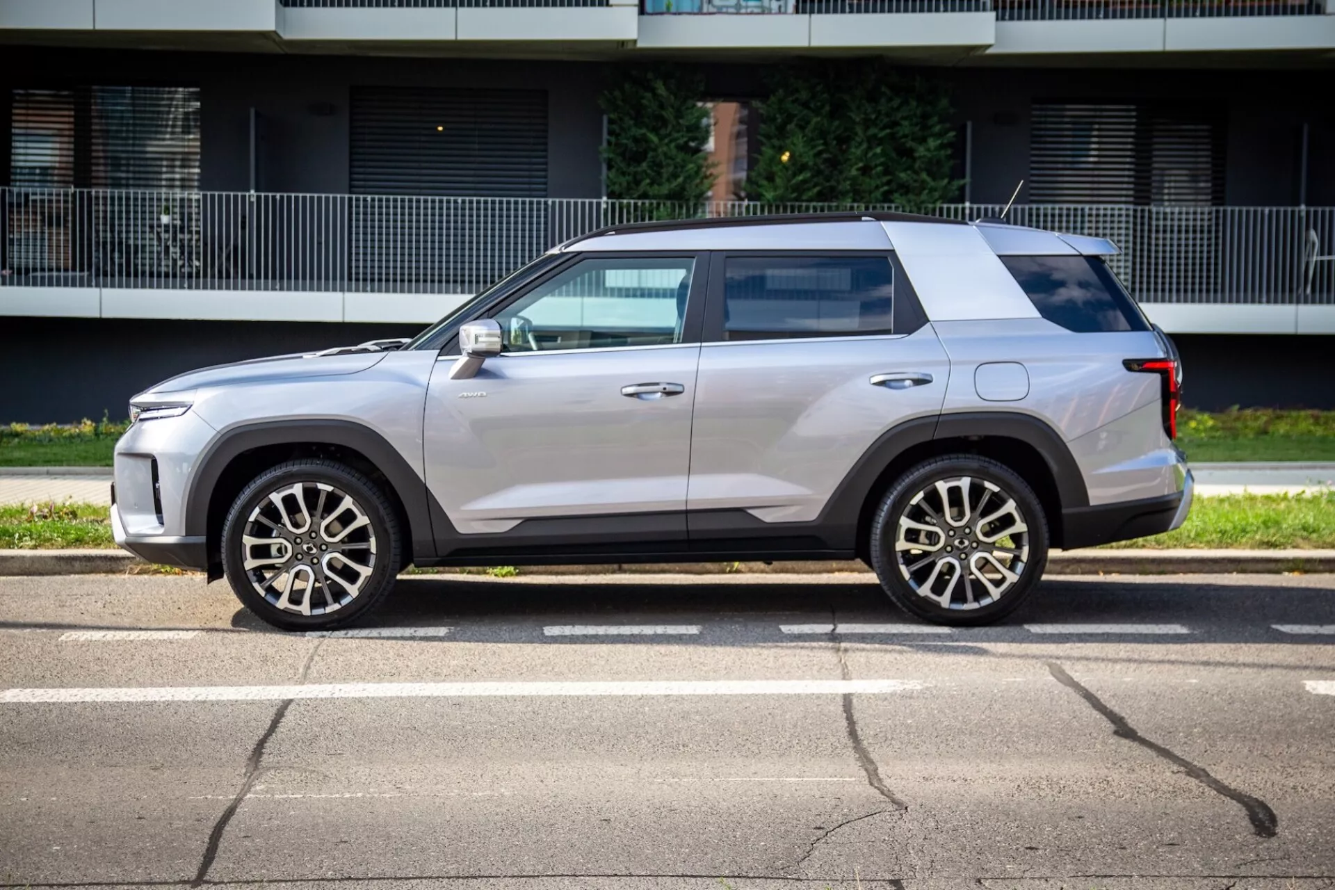 Vista lateral del SsangYong Torres 2023 mostrando su diseño cuadrado pero aerodinámico, línea de cintura alta, techo plano y pintura metálica clara con ruedas de aleación de cinco radios, espejos laterales del color de la carrocería con señales de giro integradas, ligero tinte en las ventanas, manijas de las puertas al ras y revestimiento negro en una calle soleada