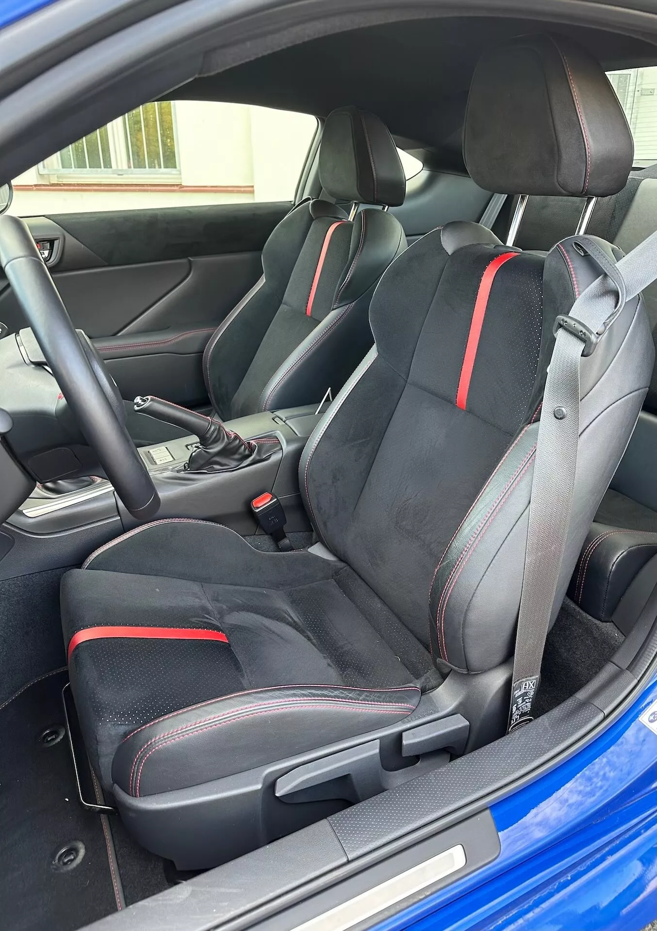 Vista interior del Subaru BRZ 2023 destacando los asientos deportivos delanteros con diseño ergonómico y detalles en rojo, selector de transmisión automática y estética moderna del cockpit desde una perspectiva exterior oblicua