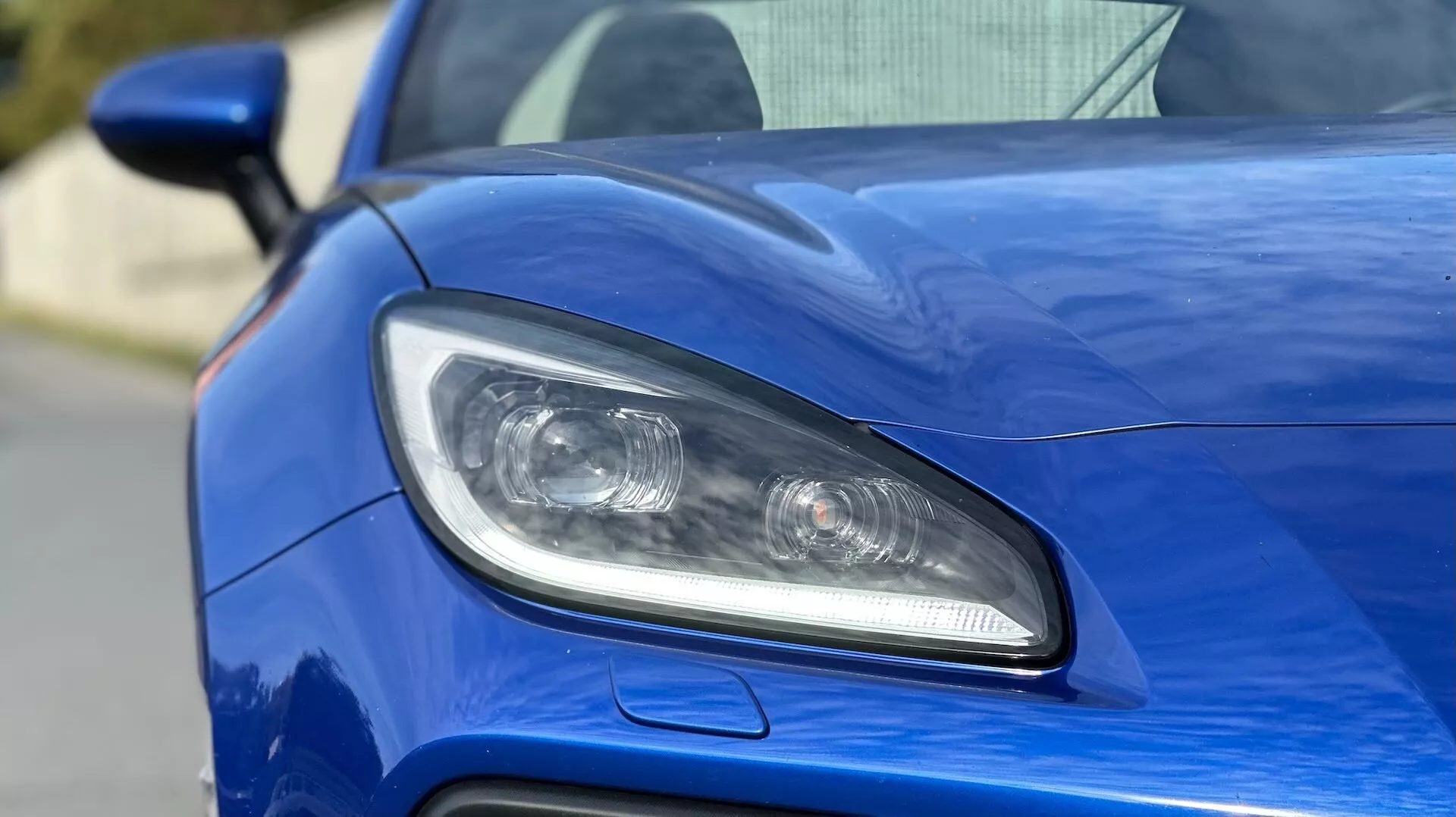 Primer plano del faro lateral del conductor del Subaru BRZ 2023, mostrando diseño de iluminación LED o HID, lentes proyectoras, y una entrada de aire deportiva contra una carrocería azul metálico