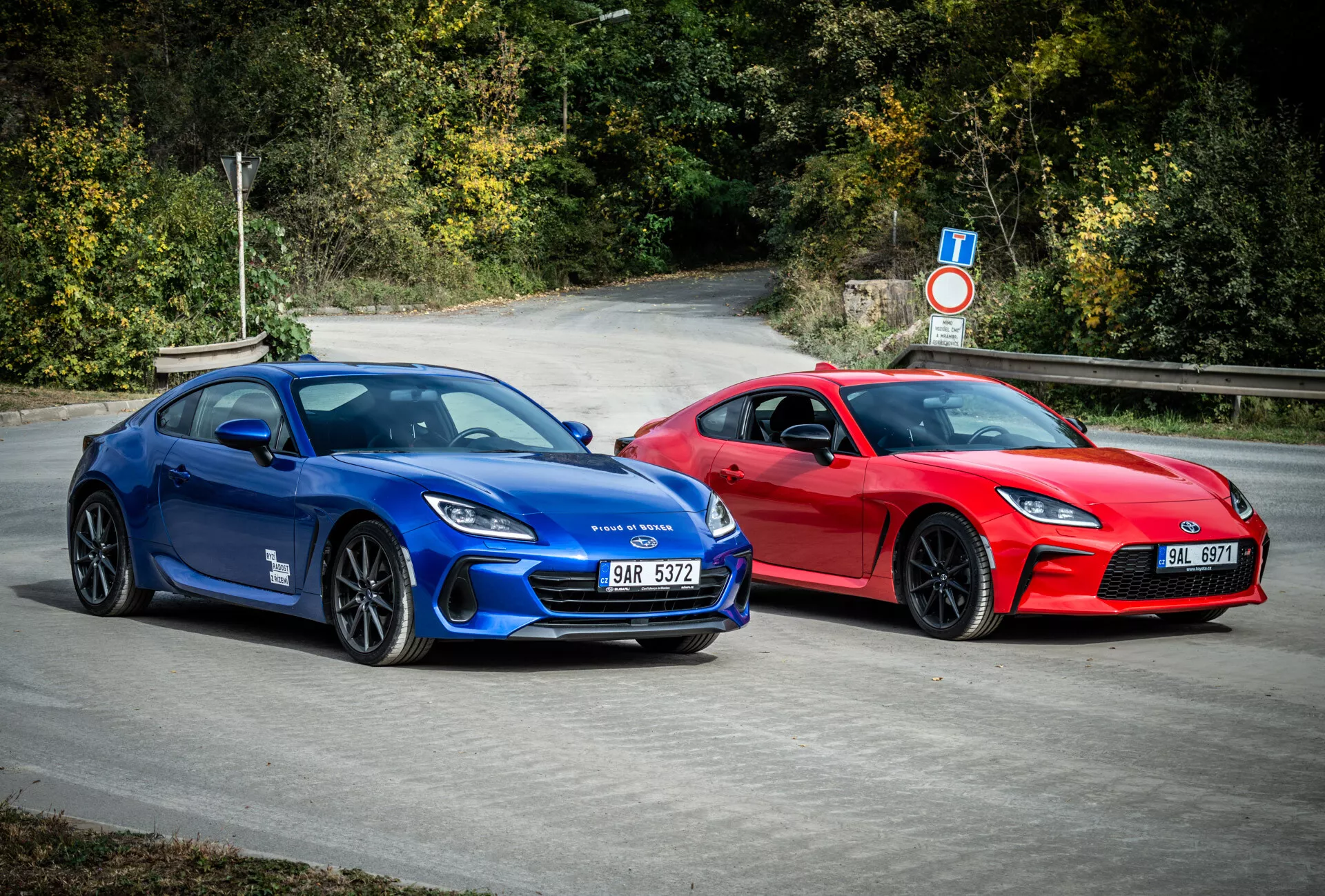 Coupés deportivos Subaru BRZ 2023 en azul y rojo con diseño aerodinámico y características de rendimiento, estacionados al aire libre rodeados de follaje natural
