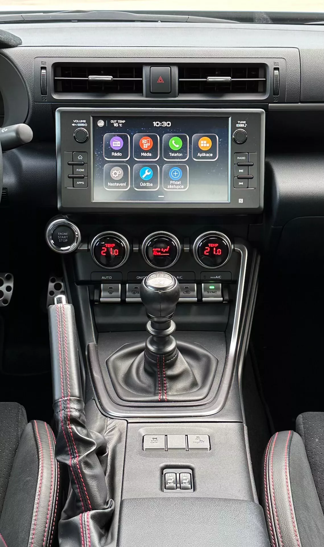 Interior del Subaru BRZ 2023 mostrando la consola central, con pantalla táctil de infotenimiento, indicador de luz de advertencia, ventilaciones de aire metálicas, control de clima de doble zona, palanca de cambios manual con cubierta de cuero, controles de calentador de asientos y un selector de modo de conducción múltiple en un diseño moderno negro y metálico.