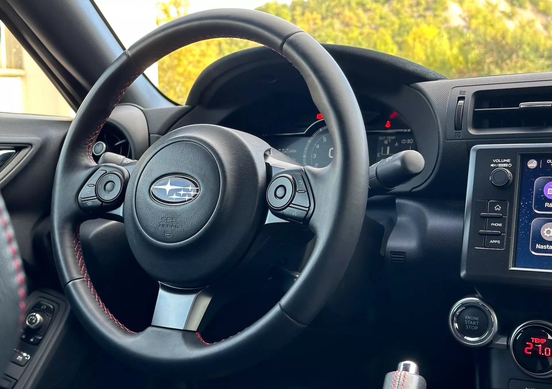 Vista interior del Subaru BRZ 2023 desde la perspectiva del pasajero mostrando el volante con acentos metálicos y logo de Subaru, botones de control, costuras contrastantes, clúster de instrumentos con indicadores retroiluminados, sistema de infoentretenimiento en consola central, controles de audio y clima, y compartimiento de almacenamiento.