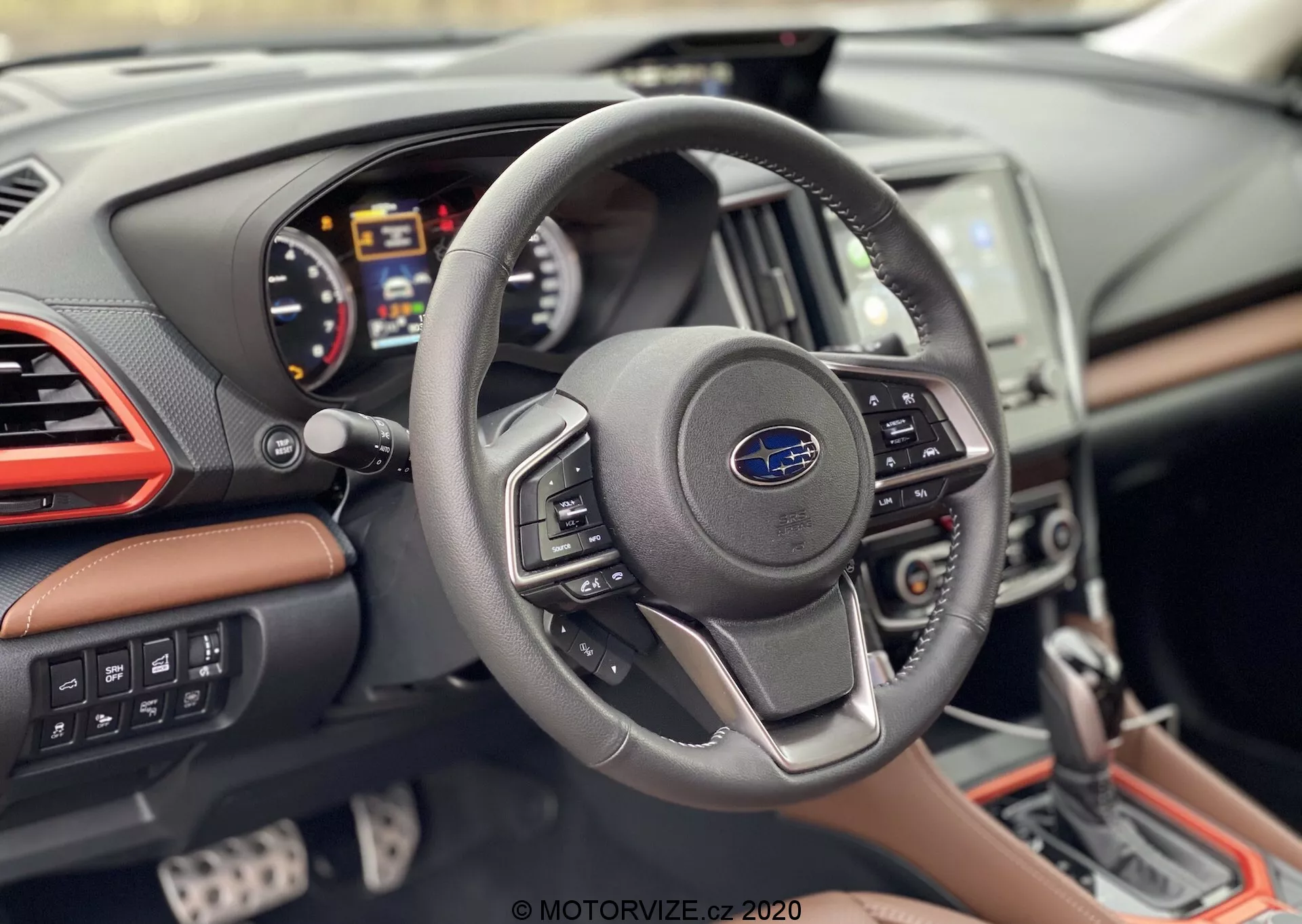 Vista del interior del Subaru Forester 2020 enfocada en la perspectiva del conductor, mostrando un volante moderno de tres radios con logotipo de Subaru y botones de control, panel de instrumentos digital con tacómetro, velocímetro y pantalla de información múltiple, consola central parcialmente visible con sistema de infoentretenimiento con pantalla táctil y salpicadero con revestimiento de cuero, acentos cromados y costuras contrastantes.