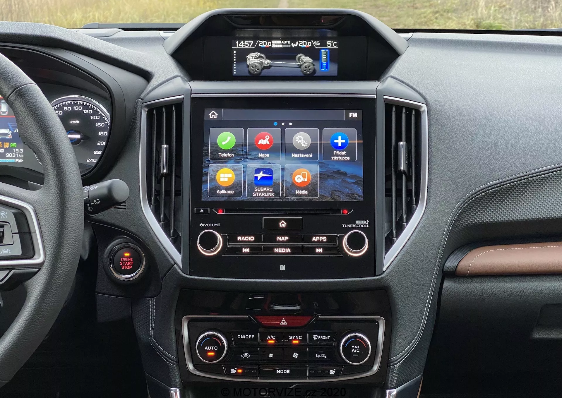 Vista interior de un Subaru Forester 2020 centrada en la consola central y el sistema de infoentretenimiento. La pantalla táctil muestra íconos coloridos para Radio, Mapa, Aplicaciones y Medios, indicando características como navegación GPS, integración de aplicaciones y reproducción multimedia. Debajo de ella, se ven los controles de clima de doble zona. Un destello de la zona del conductor revela un dial rojo, posiblemente el botón de arranque/parada del motor. El diseño interior presenta materiales similares a cuero oscuros y marrones con costuras, proporcionando una sensación de lujo.