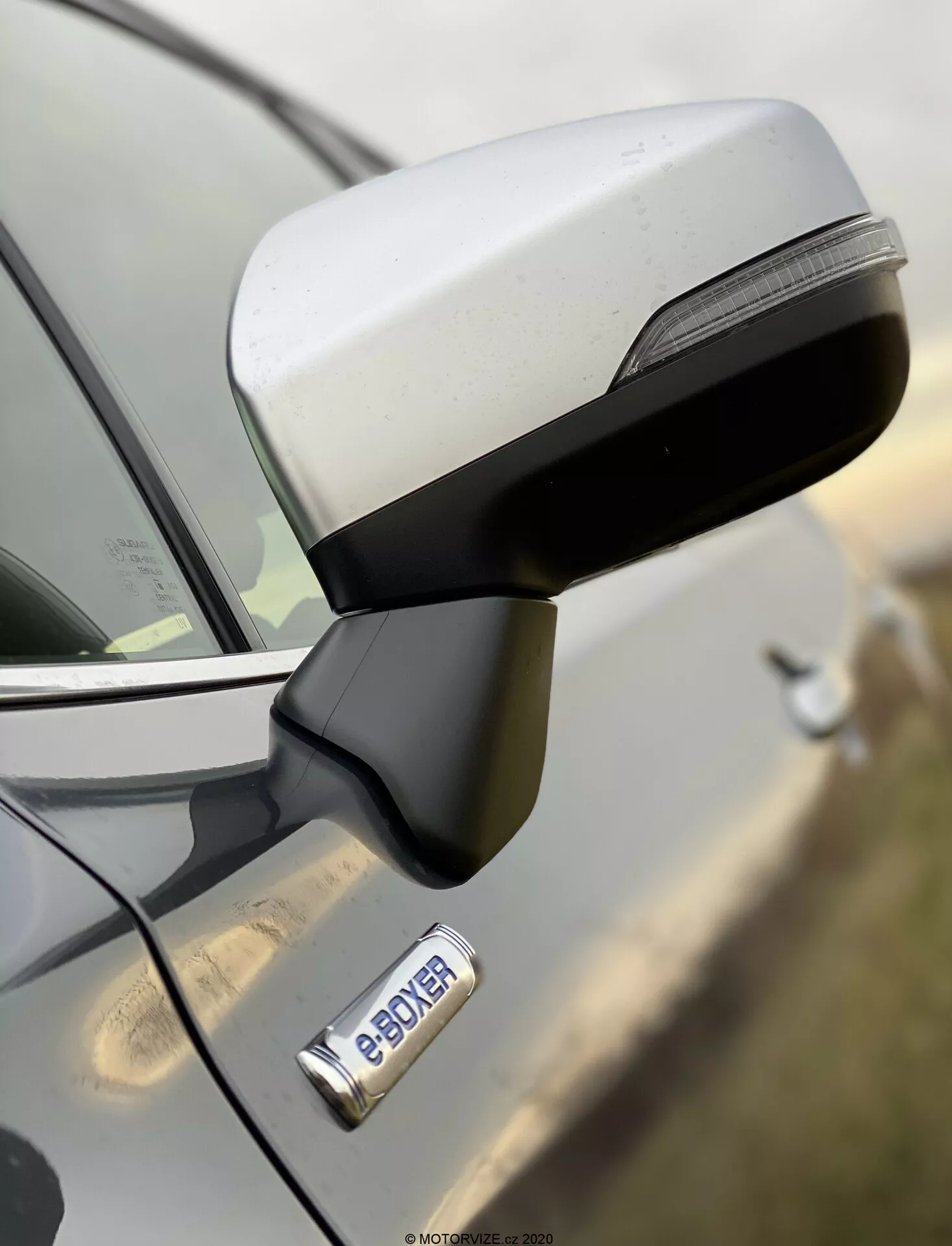 Primer plano del espejo lateral y la puerta delantera de un Subaru Forester 2020 desde una vista lateral, destacando el diseño aerodinámico del espejo con señales de giro LED integradas y la manija de la puerta cromada con botón de entrada sin llave. La insignia 'e-POWER' indica la motorización híbrida o eléctrica del vehículo. Imagen de alta resolución con poca profundidad de campo, destacando el espejo y la insignia mientras el fondo está desenfocado.