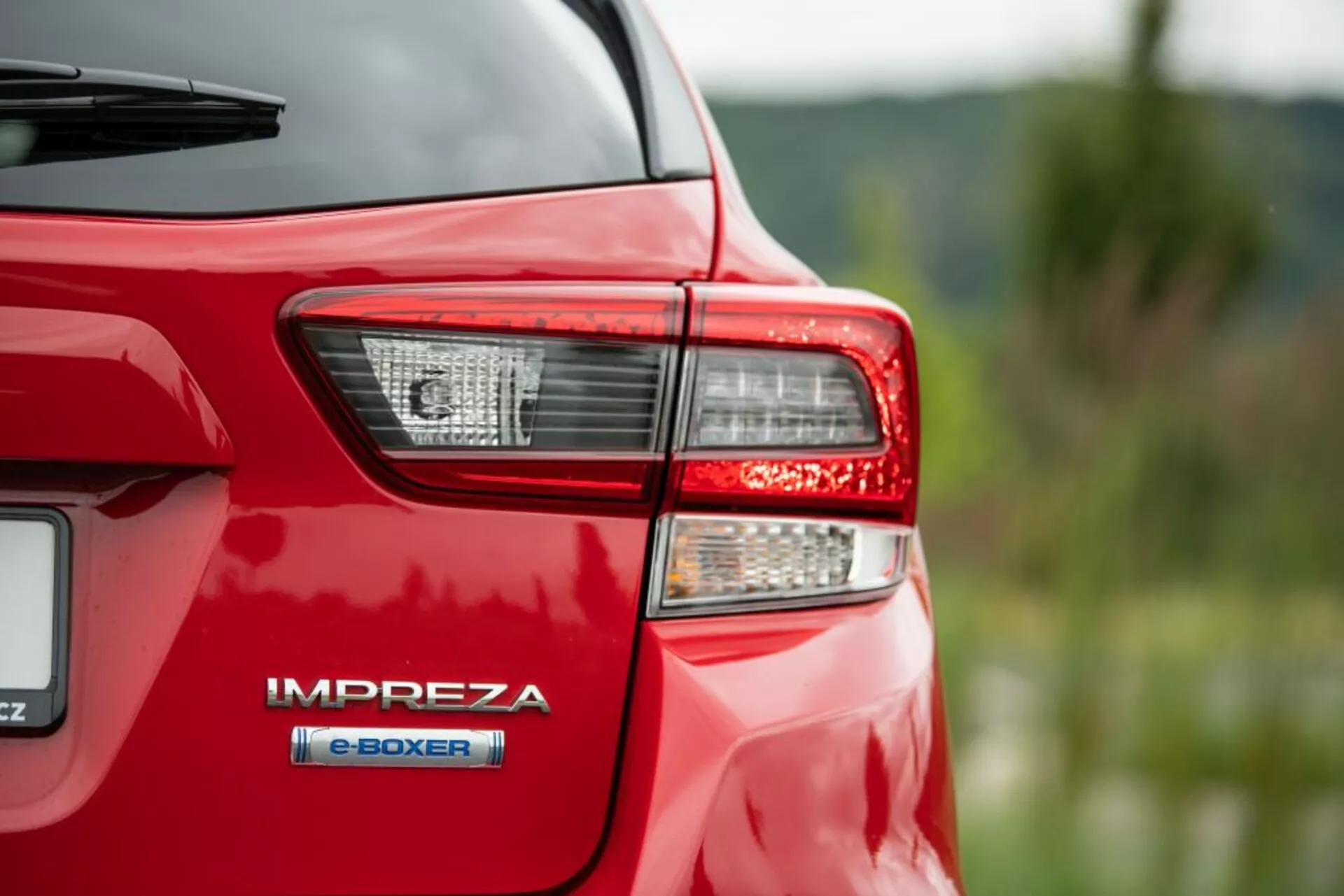 Vista detallada de la parte trasera izquierda de un Subaru Impreza rojo de 2018, mostrando un ensamblaje de luz trasera detallado con tecnología LED y la insignia del tren motriz híbrido e-BOXER