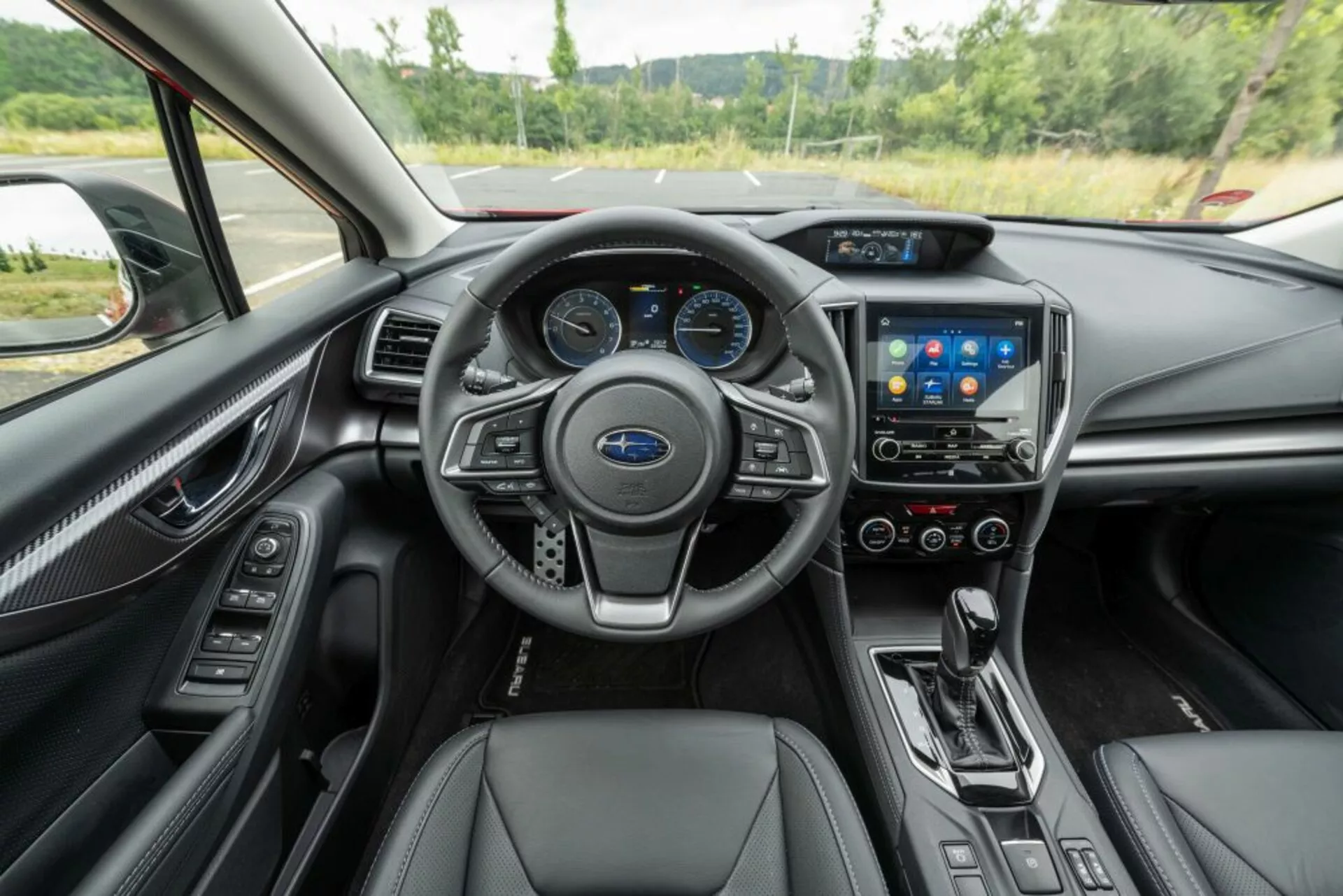 Vista interior del Subaru Impreza 2018 mostrando volante con controles, cuadro de instrumentos digital, sistema de infoentretenimiento táctil, controles climáticos, palanca de cambios automática, y asientos de cuero con acabados premium desde la perspectiva del conductor