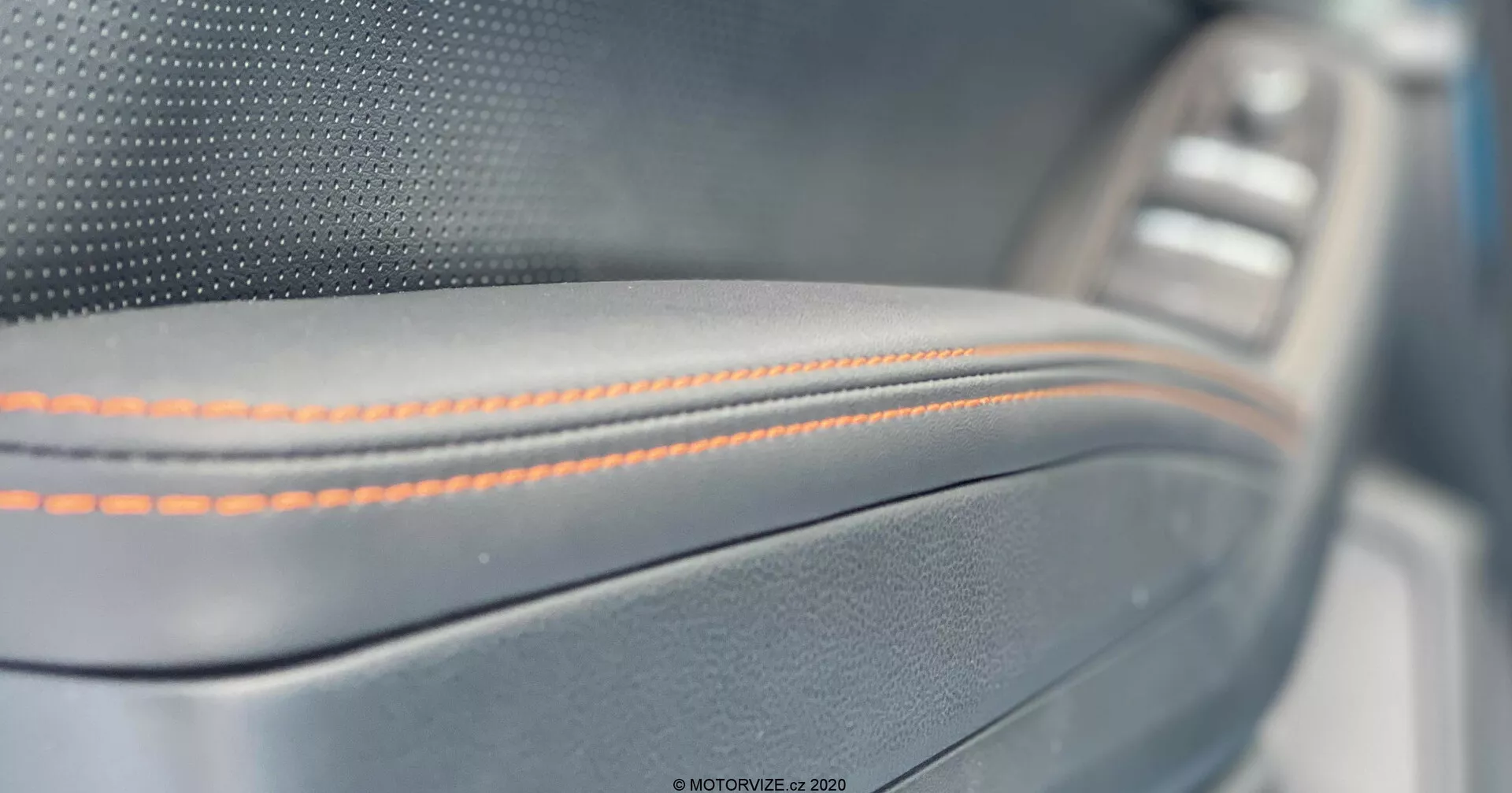Primer plano del panel de la puerta interior del Subaru XV 2018, con una costura naranja precisa en un material parecido al cuero con un adorno metálico y un panel de control de la ventana ligeramente borroso en el fondo, que muestra una artesanía premium y detalles de lujo.