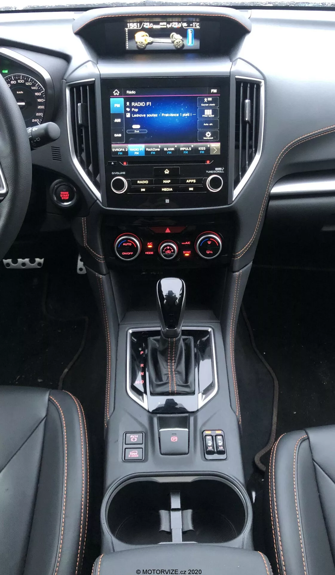 El interior de un Subaru XV 2018 (subaru-xv-1-6i-trend-lineartronic) mostrando la consola central y el tablero desde la perspectiva del asiento trasero, con un sistema de infoentretenimiento elevado y menús visibles, control climático de doble zona, selector de marchas automático ergonómico, diseño contemporáneo de materiales, portavasos y pequeños espacios de almacenamiento, varios botones de control y un volante multifuncional.