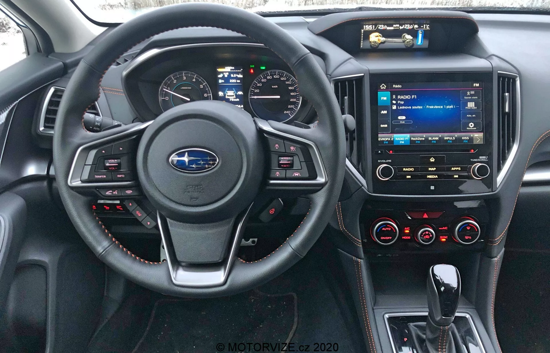 Vista interior del Subaru XV 2018 desde la perspectiva del asiento del conductor, mostrando el logo de Subaru en el volante con botones de control, detalle de costura roja, panel de instrumentos digital, sistema multimedia con pantalla táctil en la consola central, diales de control de clima, puertos USB, entrada de audio de 3.5 mm y materiales similares al cuero con costuras rojas en el tablero y paneles de las puertas.