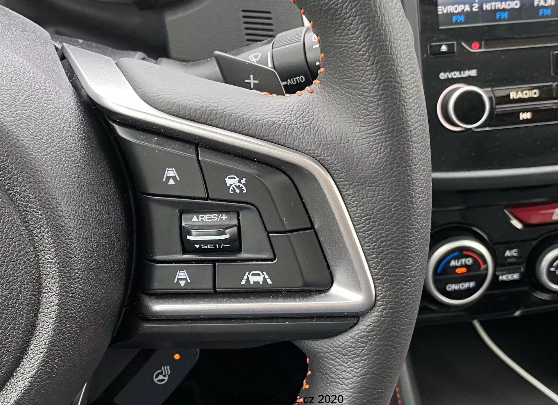 Vista de primer plano de los controles del lado izquierdo del volante de un Subaru XV 2018, que incluye botones para el Control de Crucero Adaptativo, Limitador de Velocidad, Comando de Voz y Asistencia de Mantenimiento de Carril. La toma está hecha desde el asiento del conductor, destacando los símbolos iluminados en una superficie de plástico negro, con parte del tablero y la consola central visible en el fondo.