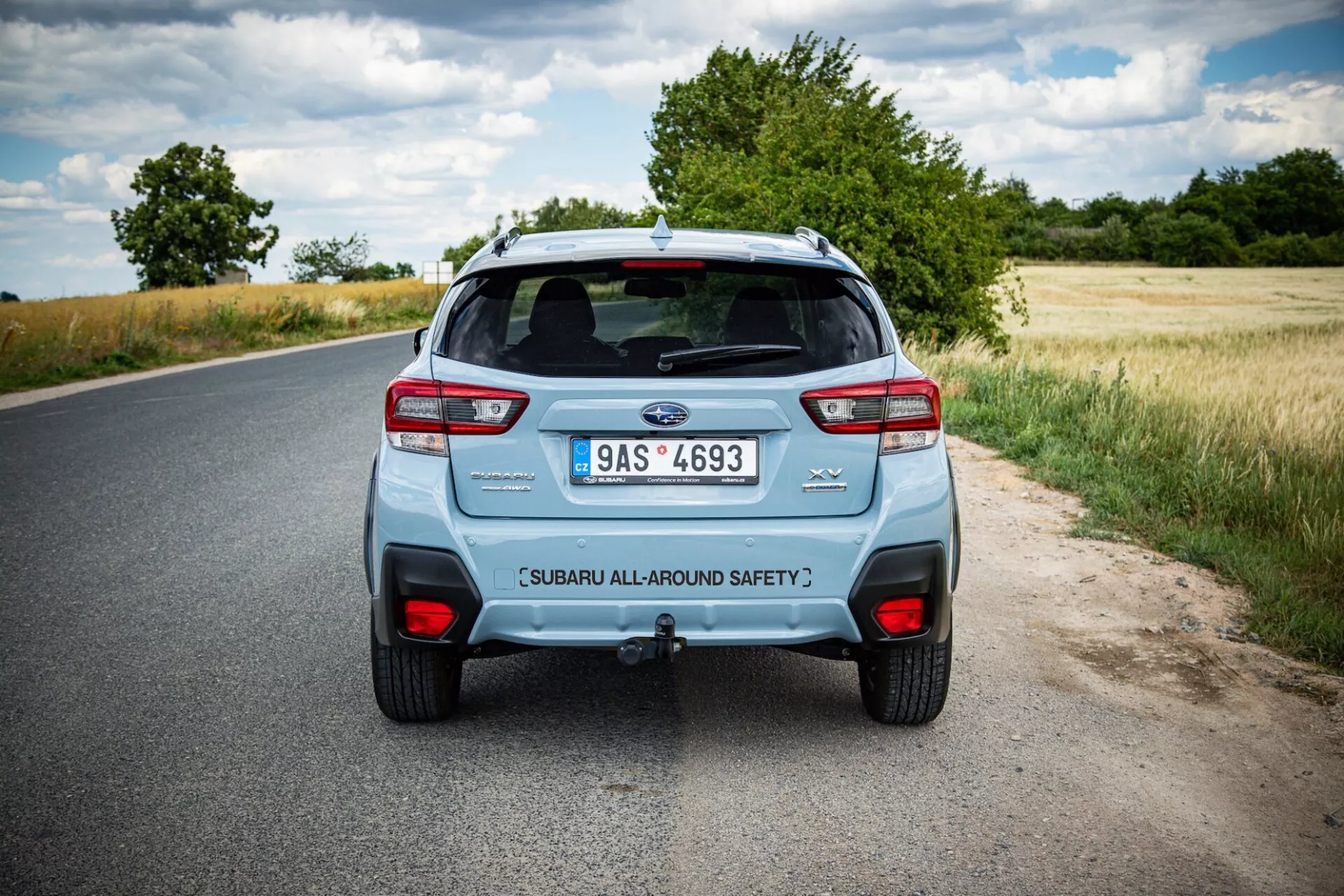 Vista trasera de un Subaru XV 2021 en una carretera rural, mostrando las luces traseras distintivas del coche, sistema de doble escape y portón trasero etiquetado de seguridad bajo cielos parcialmente nublados