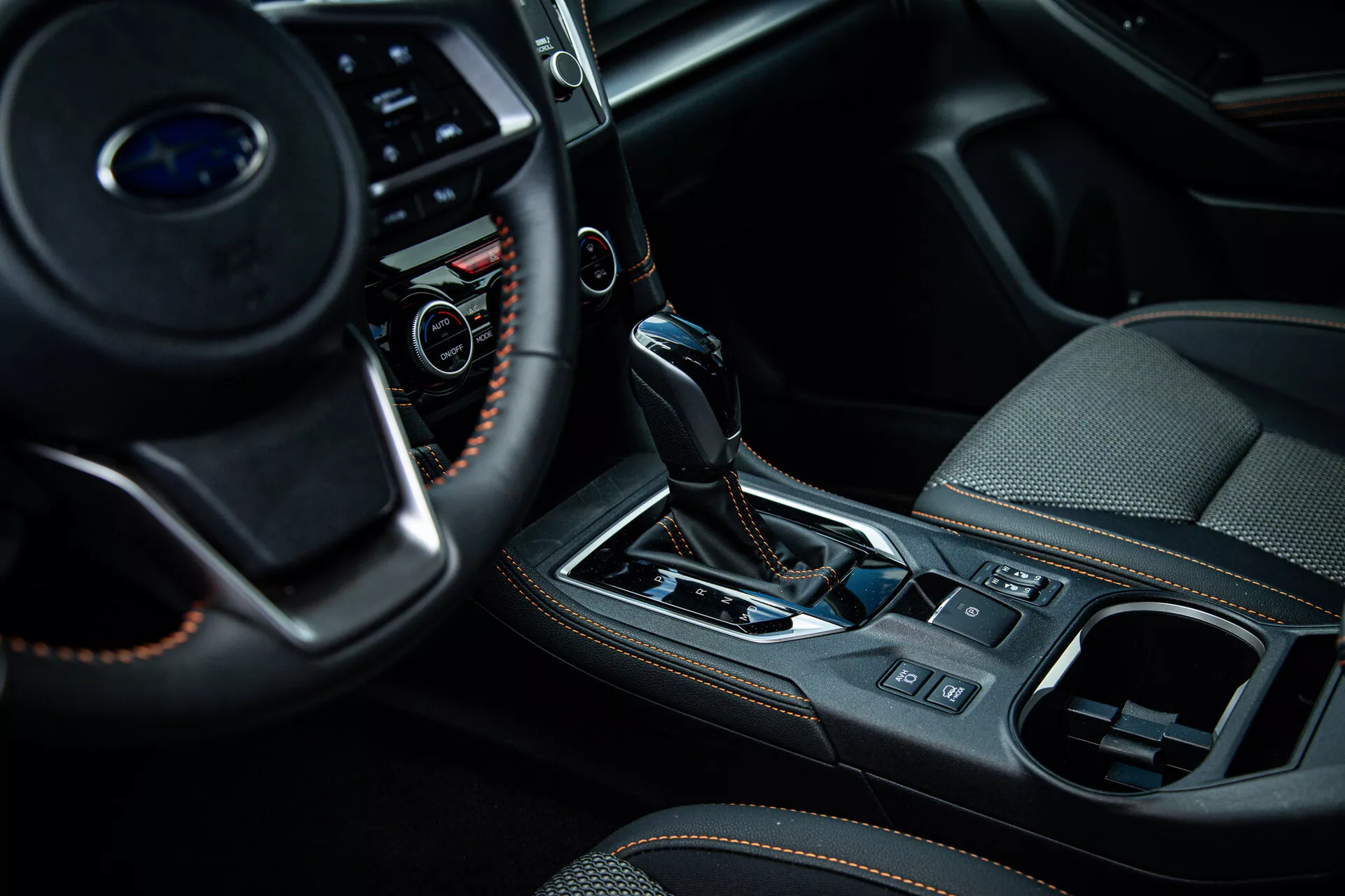 Vista cercana del interior de un Subaru XV 2021 enfocando la consola central y el área del cambio de marchas desde una perspectiva del lado del pasajero, mostrando botones multifunción en el volante, palanca de cambios automática con funda de cuero y acentos metálicos, y características de diseño interior de alta gama como el freno de estacionamiento electrónico y el sistema de control climático.