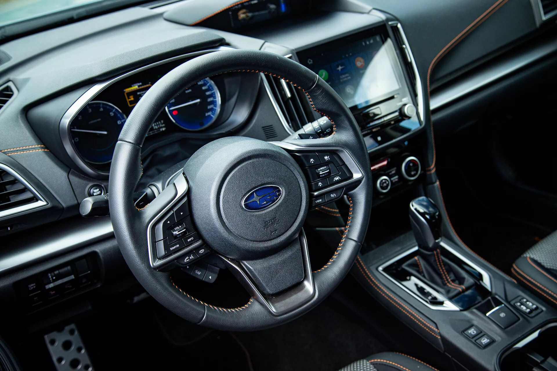 Vista interior del Subaru XV 2021 desde el lado del pasajero delantero mostrando volante de tres radios con controles multifunción, cuadro de instrumentos con pantallas analógicas y digitales en el tablero, sistema de infoentretenimiento táctil central, botones de control del clima, palanca de cambios automática, y materiales de acabado de lujo, incluyendo cuero y acentos de cromo.