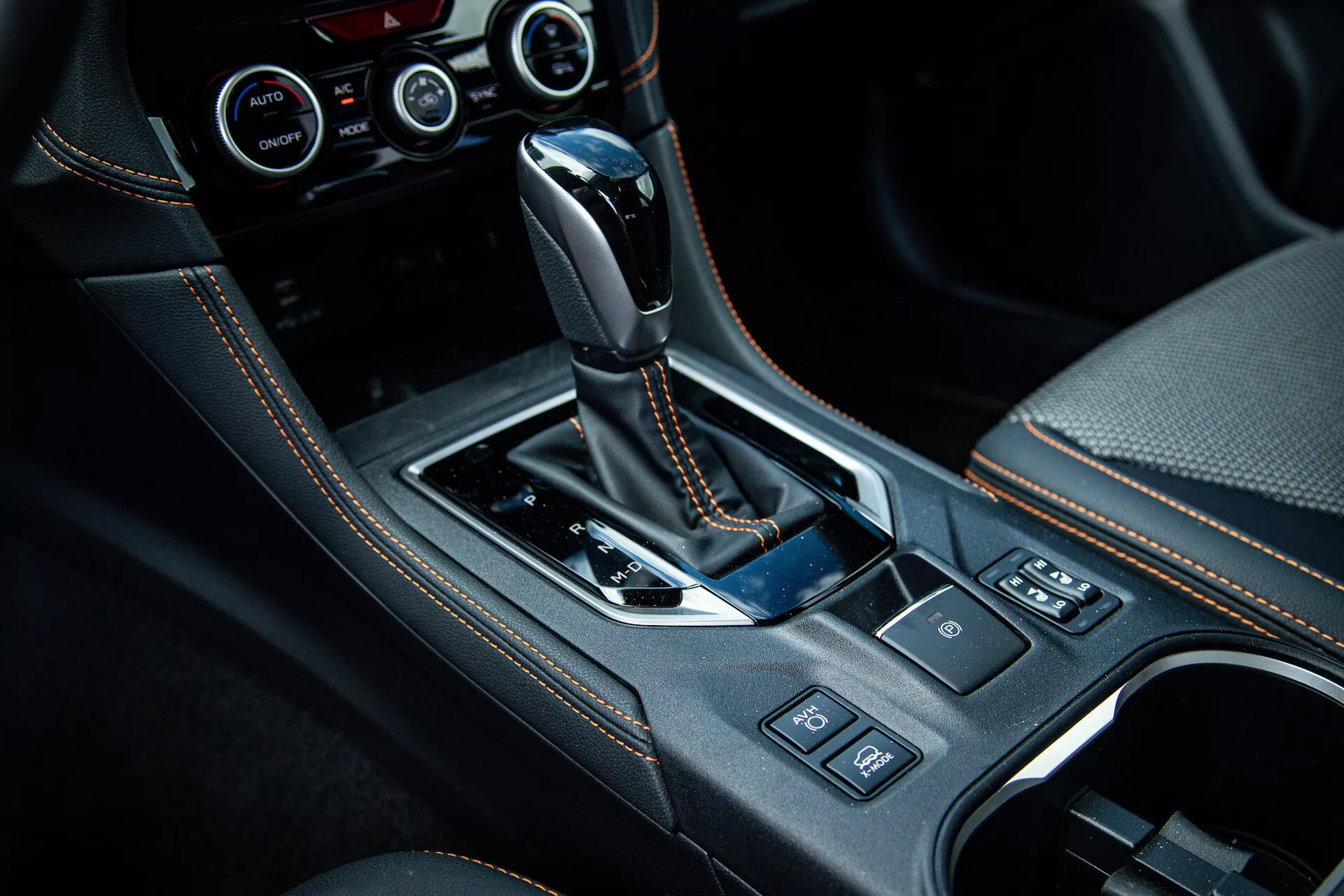 Consola central del Subaru XV 2021 con palanca de cambios automática envuelta en cuero, panel en negro brillante, detalles cromados, portavasos, botones de control y sistema de control climático avanzado visible en foto de interior de alta calidad