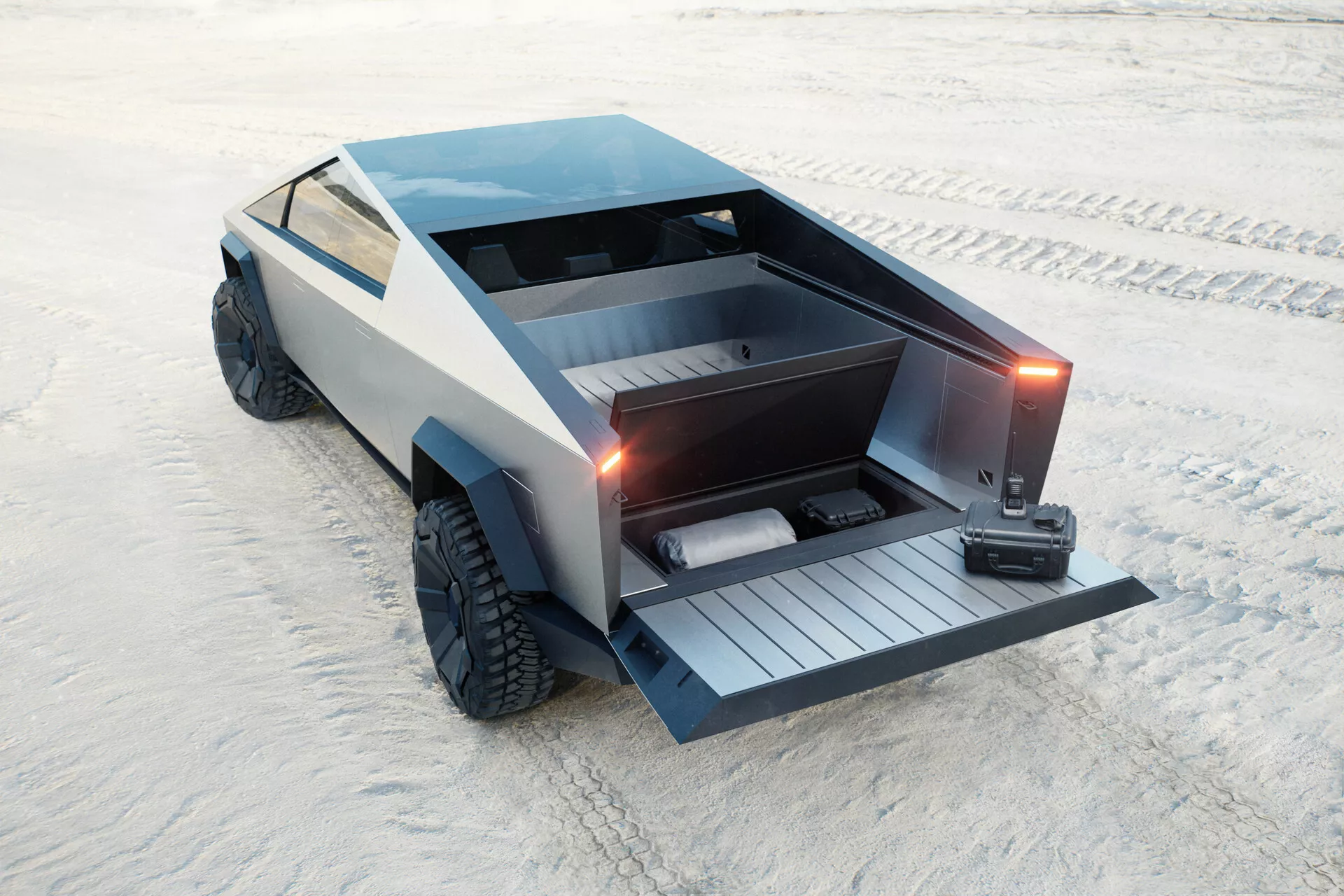 Futurista Tesla Cybertruck 2021 (1ra generación) estacionado en una superficie arenosa, capturado desde una vista elevada de tres cuartos trasera. El diseño angular y poligonal presenta una caja plana con una puerta trasera motorizada abaida, revelando una rampa incorporada. El vehículo también incluye una cubierta de tonelón bloqueable, grandes llantas todoterreno y un acabado gris mate que contribuye a su estética minimalista, industrial. No se ven manijas de puertas tradicionales ni espejos laterales, lo que sugiere manijas retráctiles y espejos basados en cámaras. Se especula que es eléctrico, centrándose en la practicidad y la capacidad todoterreno.