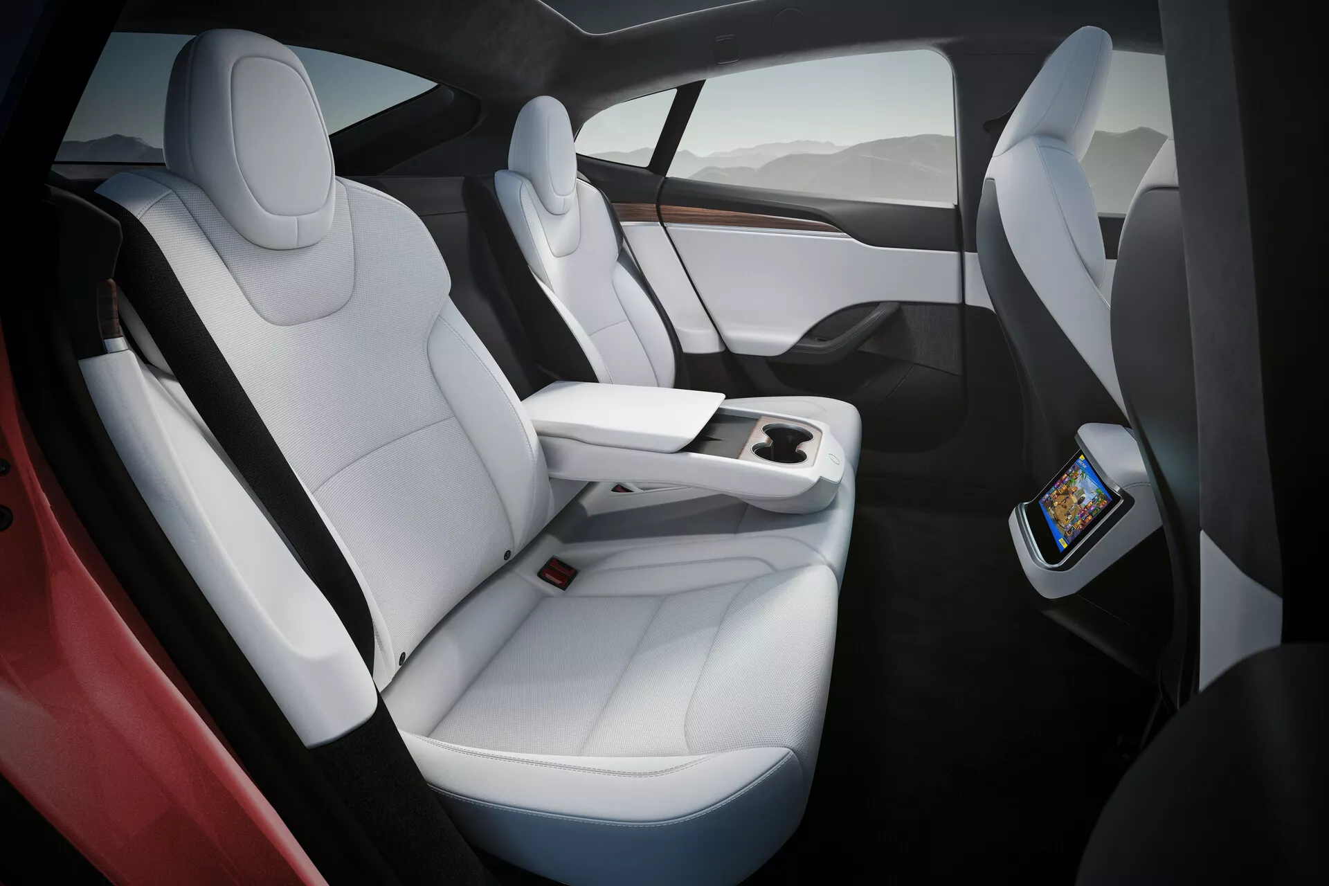 Interior del Tesla Model S 2016 (1ª generación facelift) que muestra asientos de cuero blanco de lujo con acentos negros, diseño ergonómico y amplio espacio para las piernas. La imagen captura los asientos del lado derecho desde una perspectiva algo elevada, destacando la consola central funcional que termina antes de los asientos traseros, con una pantalla táctil para los pasajeros traseros y carga inalámbrica para smartphones. Techo panorámico de cristal que ofrece luz natural y una sensación de amplitud.