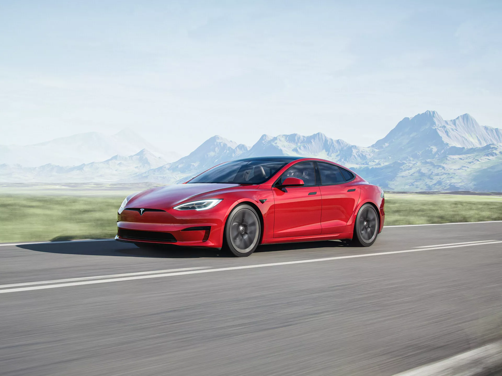 Imagen de perfil lateral de un sedán eléctrico Tesla Model S 2016 (1ª generación facelift) en rojo, capturado en movimiento. Se muestra el diseño elegante y aerodinámico del automóvil, con líneas suaves desde el guardabarros delantero hasta el extremo trasero y llantas pulidas. Fotografía tomada en una carretera de asfalto con un fondo borroso de montañas y un cielo despejado, enfatizando la velocidad y el movimiento del vehículo.