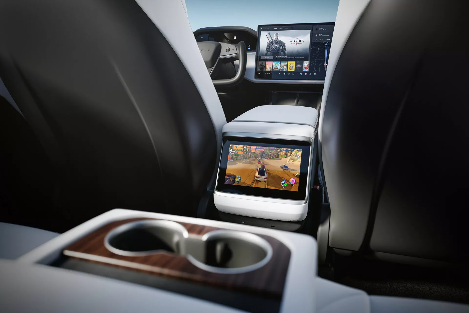 Vista interior del Tesla Model S 2016 (primera generación facelift) centrada en el compartimento trasero. Perspectiva desde el asiento trasero a la altura del cojín mostrando dos asientos delanteros con reposacabezas, consola central y pantalla incorporada en el respaldo del asiento delantero del pasajero. Tecnología de entretenimiento en los asientos traseros evidente con pantalla activa mostrando contenido multimedia. Características incluyen reposabrazos plegable con portavasos integrados y acabado en madera, visión parcial del tablero delantero con pantalla de infoentretenimiento más grande y materiales de lujo. Interior bien iluminado con tonos neutros que indican un vehículo de lujo contemporáneo.