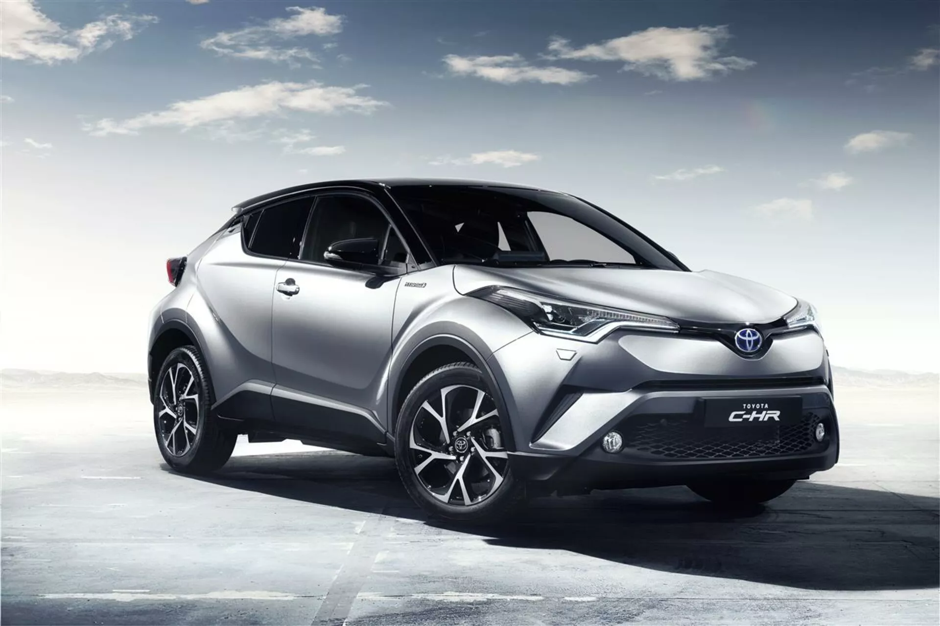 SUV crossover Toyota C-HR 2016 mostrado en un paisaje abierto renderizado digitalmente con un cielo nublado, destacando su alta distancia al suelo, modernos faros LED, llantas de aleación deportivas y cuerpo esculpido aerodinámicamente para un mejor rendimiento y eficiencia.