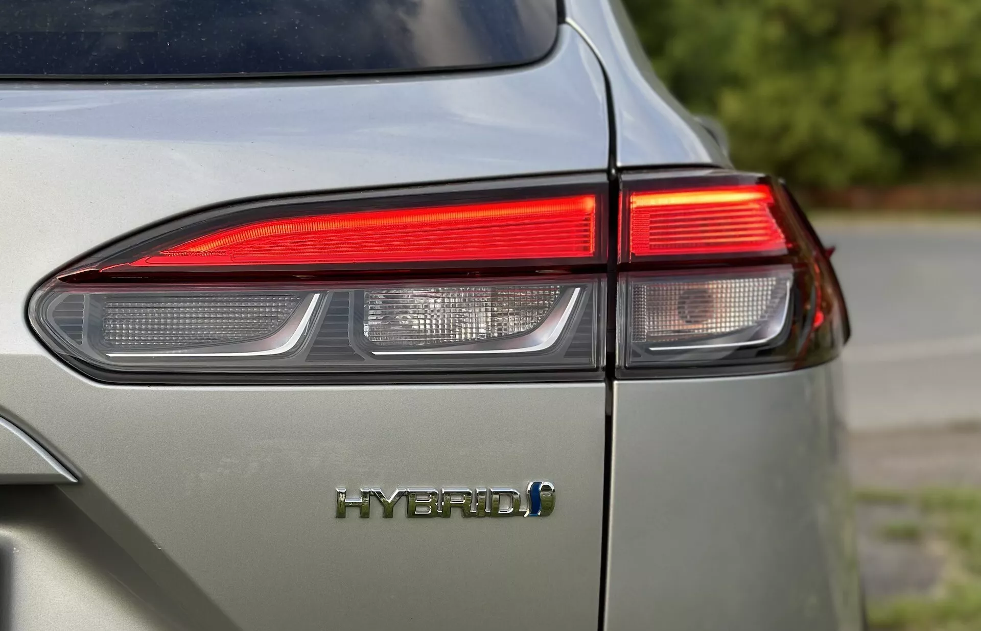 Primer plano de la esquina trasera izquierda del Toyota Corolla-Cross 2022 mostrando el diseño de luz trasera LED y el emblema HYBRID con enfoque en la tecnología ecológica del vehículo y acabado brillante en color gris claro apagado