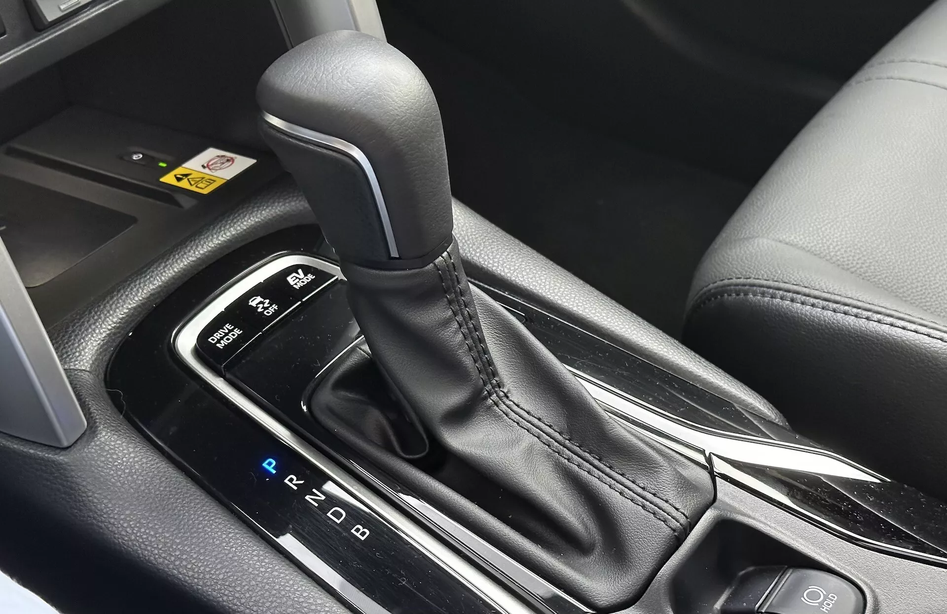 Vista interior detallada del Toyota Corolla Cross 2022 mostrando la palanca de cambios automática con disposición PRND visible, rodeada por una consola central elegante con acabados en plástico negro y acentos metálicos, destacando el diseño ergonómico y las características tecnológicas modernas