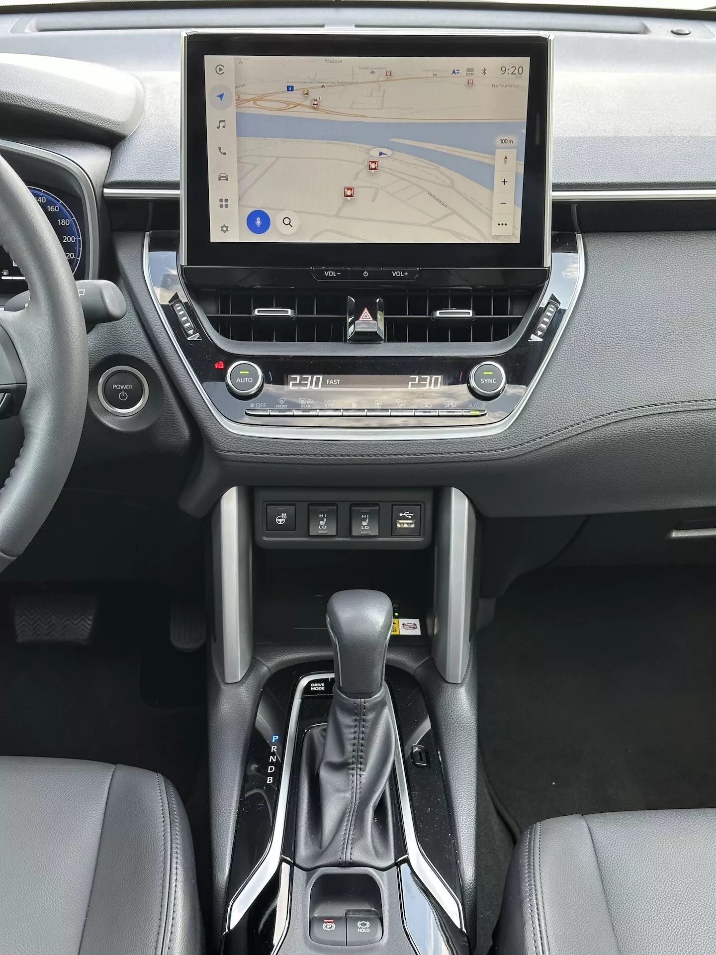 Interior del Toyota Corolla Cross 2022 con sistema de infoentretenimiento táctil con navegación GPS, control de clima bizona, ranura para CD, botones de control de medios y teléfono, palanca de cambios automática moderna y acentos de cuero en la consola central y diseño del tablero