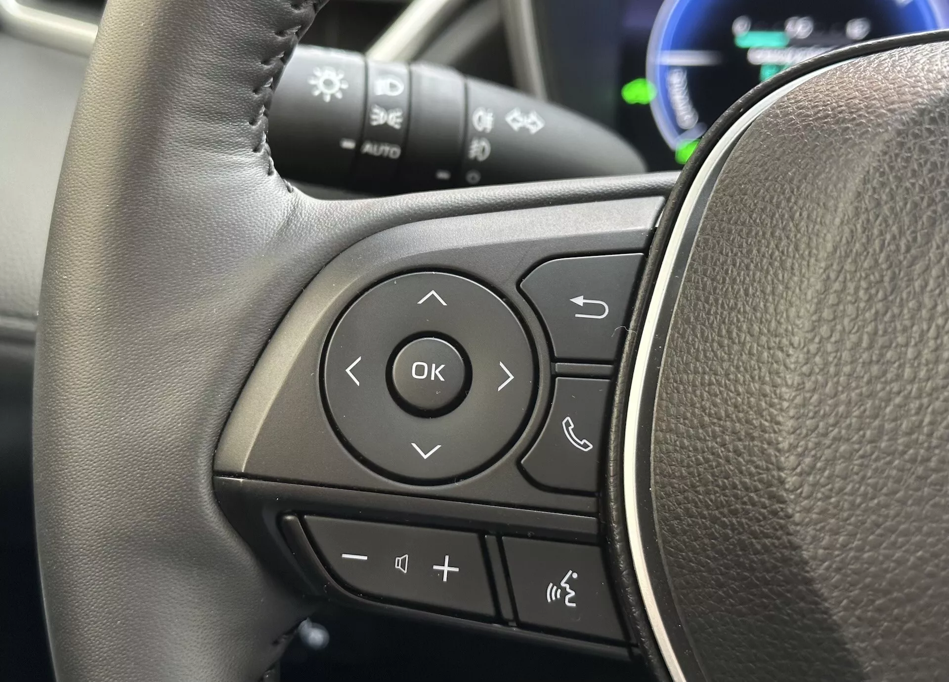 Vista detallada del volante de Toyota Corolla Cross 2022 centrada en los controles multifunción en el radio izquierdo con textura similar al cuero y botones claramente marcados para audio, conectividad telefónica Bluetooth, comandos de voz y navegación a través del sistema de información del conductor