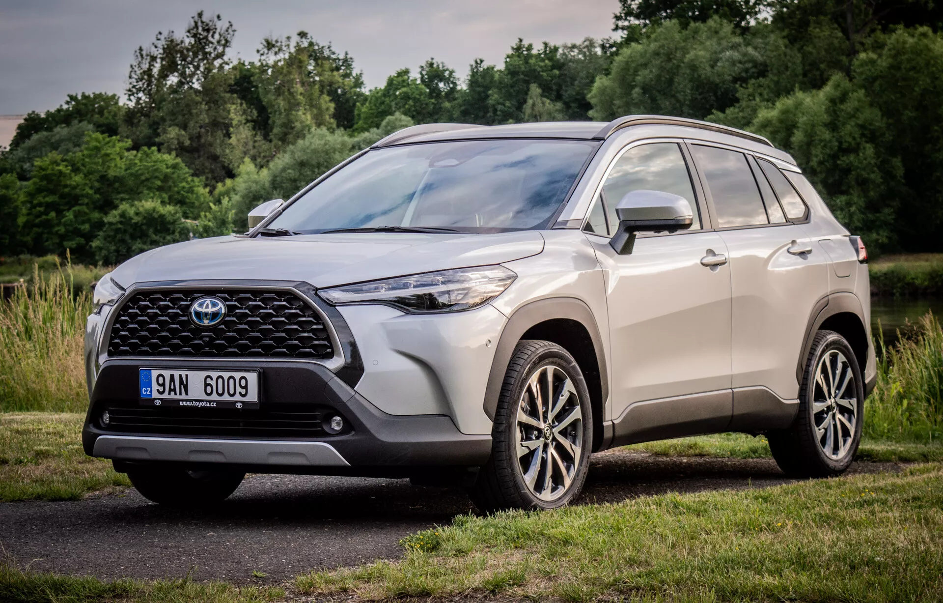 Toyota Corolla Cross 2022 mostrando su diseño dinámico con una perspectiva frontal y lateral de tres cuartos, resaltando la gran parrilla frontal estampada, unidades de faros LED elegantes y ruedas de aleación de múltiples radios, estacionado en un entorno natural
