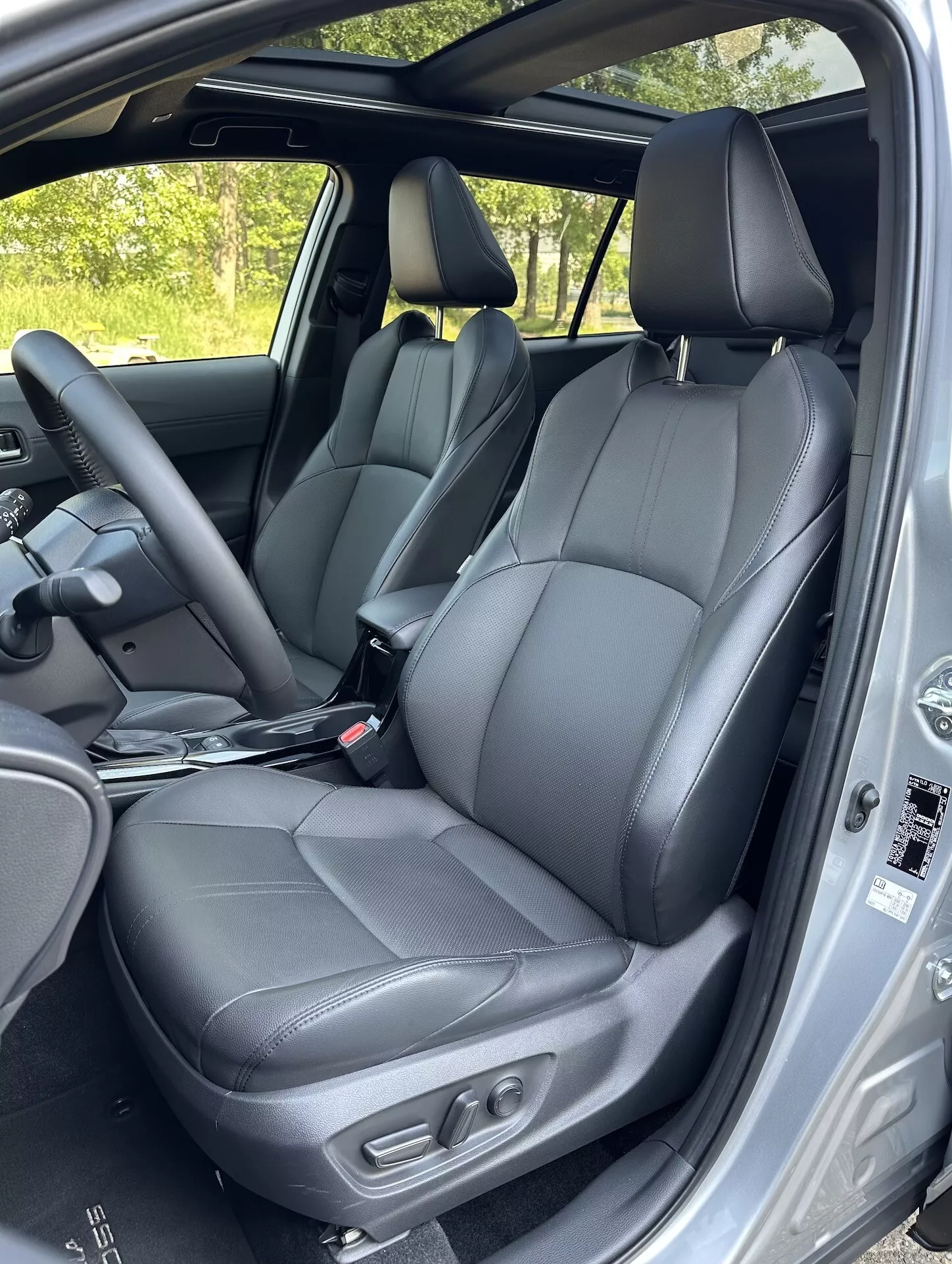 Vista interior de Toyota Corolla Cross 2022 destacando asientos delanteros de cuero negro con controles de ajuste, parte de los asientos traseros, volante y características de seguridad del marco de la puerta en luz natural del día
