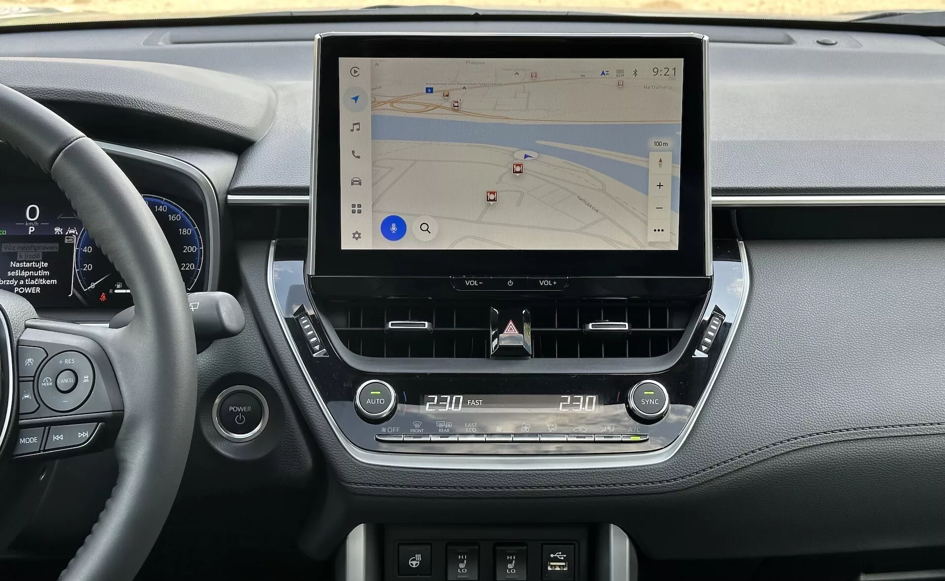 Interior de Toyota Corolla Cross 2022 mostrando una consola central moderna con una gran pantalla táctil vertical para navegación, rodeada de elegantes elementos del tablero incorporando detalles en cuero, grupo de instrumentos digitales al lado del volante y controles táctiles ergonómicos para el clima y el audio, ambientado en luz natural.