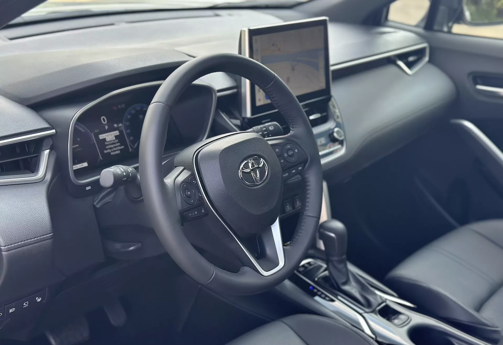 Interior del Toyota Corolla Cross 2022 enfocado en el lado del conductor con volante detallado, cuadro de instrumentos digital y pantalla táctil de infotainment central con tecnología moderna y acentos de cuero negro
