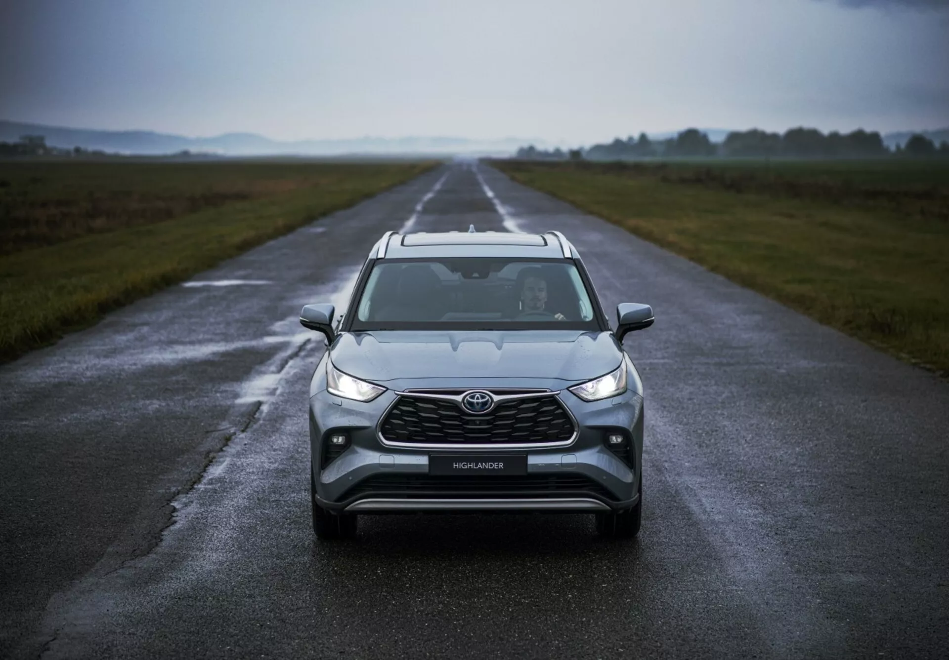Toyota Highlander 2021 posicionado en una carretera mojada destacando su diseño frontal, clima nublado, con faros LED, luces antiniebla, una parrilla grande y tecnología avanzada de seguridad