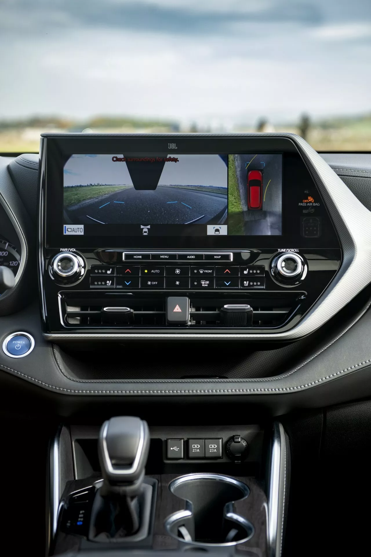 Interior del Toyota Highlander 2021 destacando la consola central con pantalla táctil orientada horizontalmente que muestra la cámara trasera y el asistente de estacionamiento, controles de clima de zona dual y palanca de cambios automática
