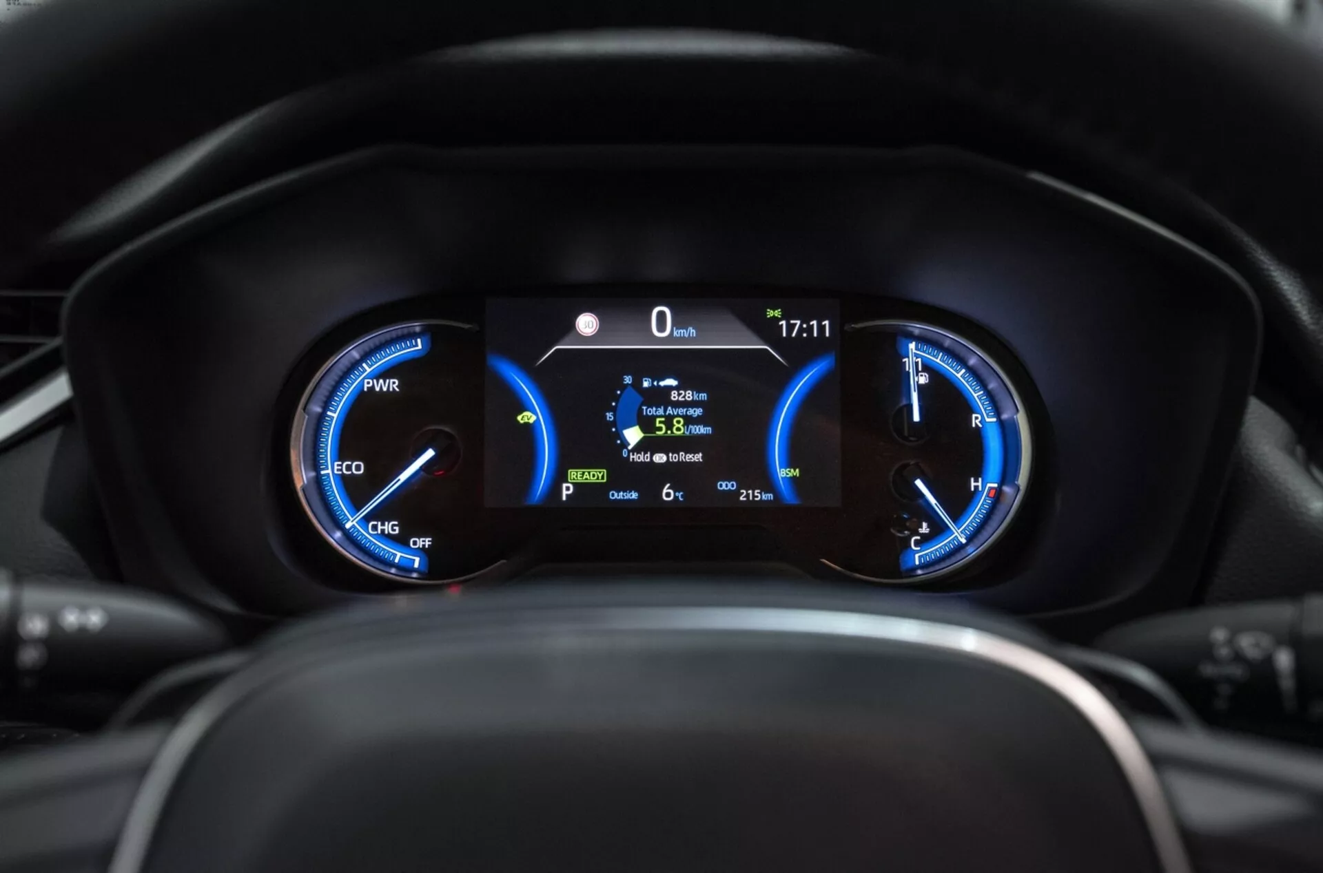 Primer plano del cuadro de instrumentos de la Toyota RAV4 2019 mostrando medidores híbridos con medidor de potencia, velocímetro y pantalla digital central que indica posición estacionaria, eficiencia de combustible y temperatura exterior desde la perspectiva del conductor.