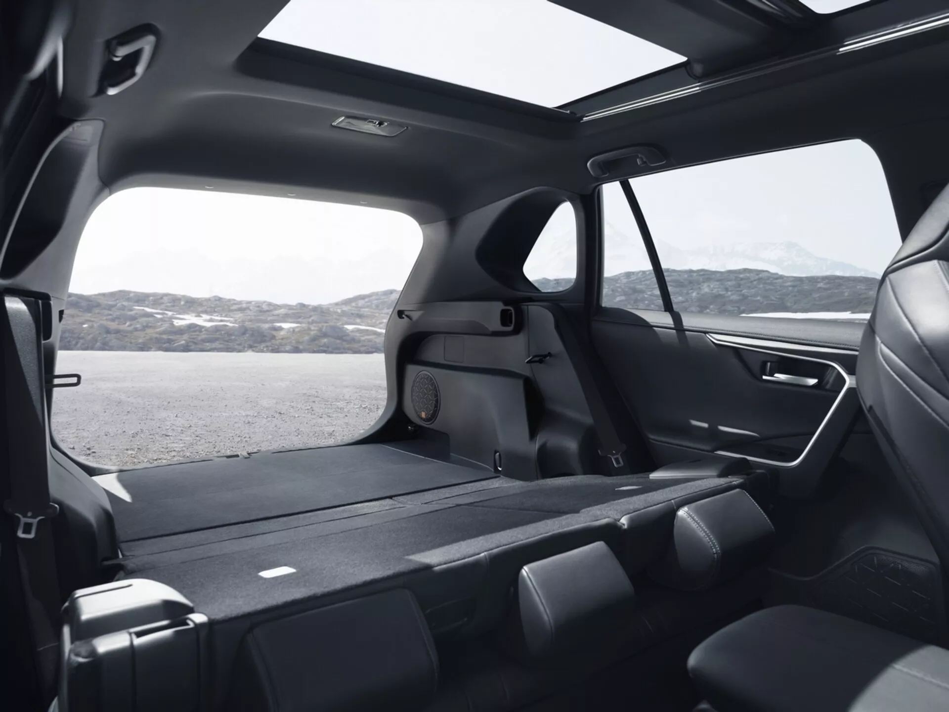 Vista interior de un Toyota RAV4 2019 mostrando la espaciosa cabina trasera desde un ángulo elevado, destacando los asientos plegables de la segunda fila, amplio espacio de carga, grandes ventanas tintadas, diseño moderno con materiales premium, techo solar panorámico, avanzado sistema de iluminación y características de control climático