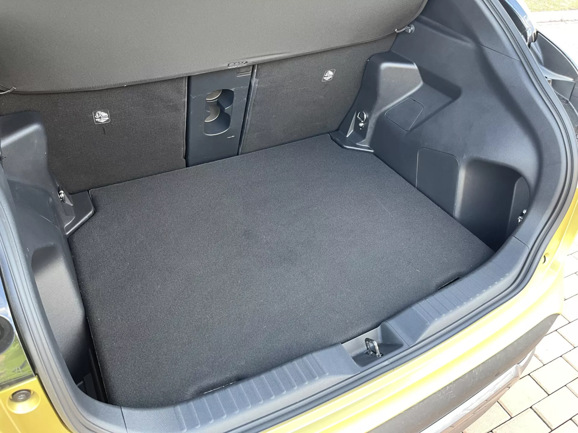 Vista interior del maletero del Toyota Yaris Cross 2021 mostrando un espacio de carga vacío, forrado con alfombra, con lados de plástico moldeado, áreas recesivas para almacenamiento, cortes de acceso a equipo y indentaciones de asientos traseros plegables