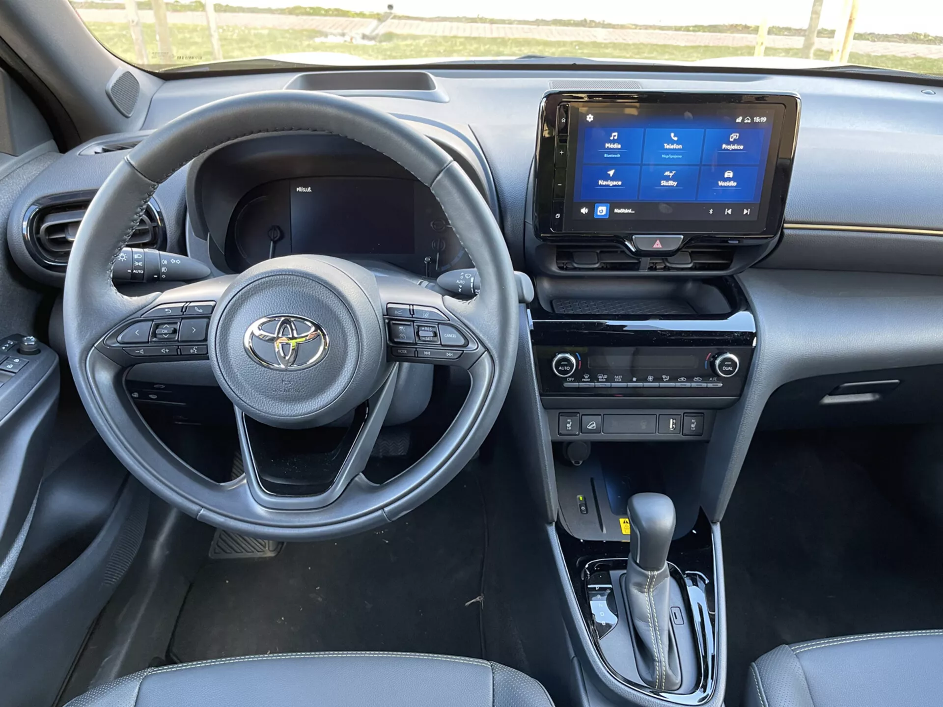 Vista interior del Toyota Yaris Cross 2021 desde el lado del pasajero delantero, mostrando el tablero, volante con controles integrados, sistema de infoentretenimiento táctil, palanca de cambios automática y características elegantes de asientos y diseño en tema oscuro
