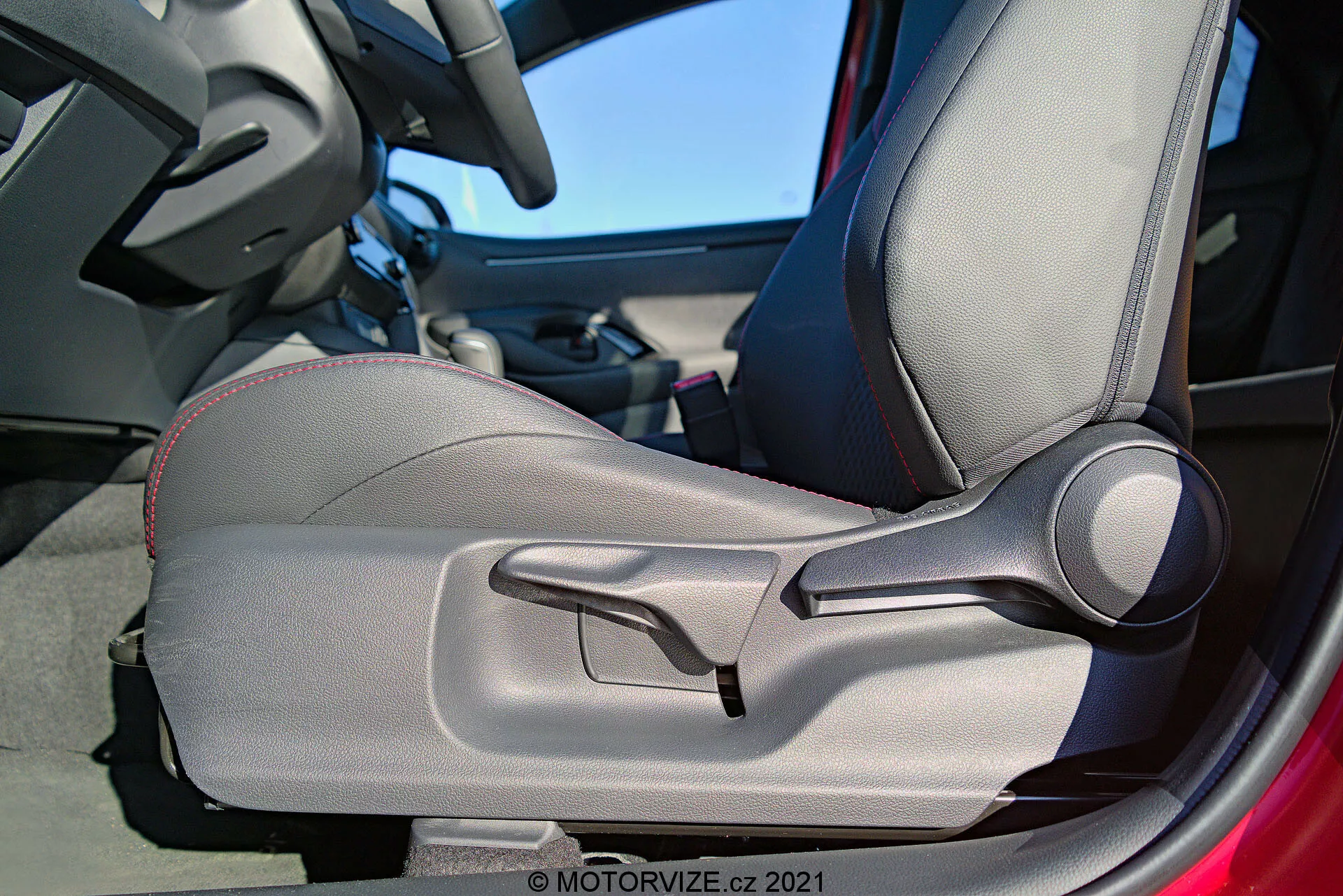 Toma de detalle interno del Toyota Yaris 2020 enfocada en la puerta y asiento del conductor, destacando la tapicería bicolor, las costuras decorativas, el diseño contorneado para soporte ergonómico, las almohadillas laterales ajustables manualmente y una palanca prominente para el ajuste manual del asiento. El marco de la puerta es parcialmente visible, sugiriendo que la puerta está abierta.